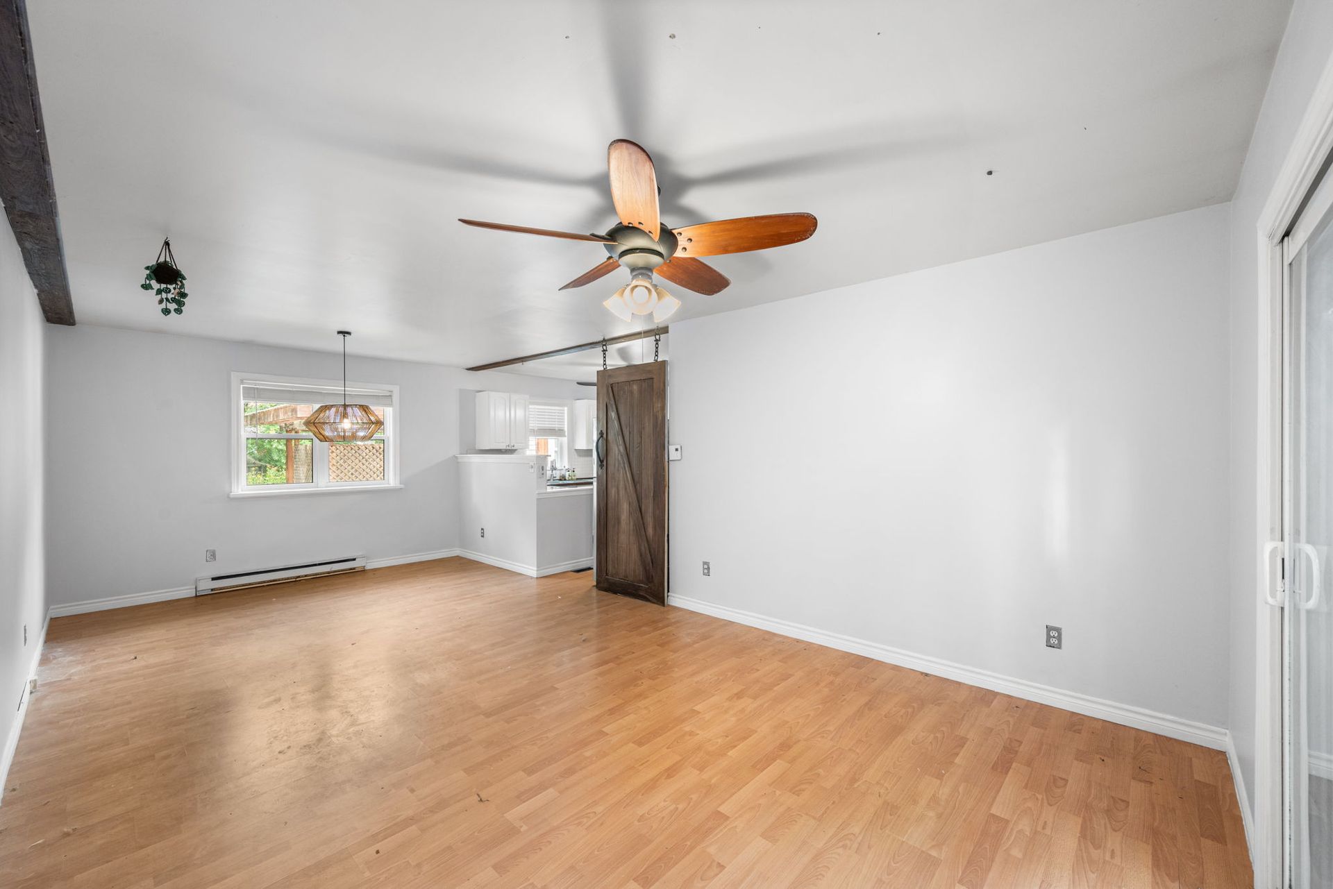 Empty living room with hardwood floor, white walls, ceiling fan, and sliding glass door.