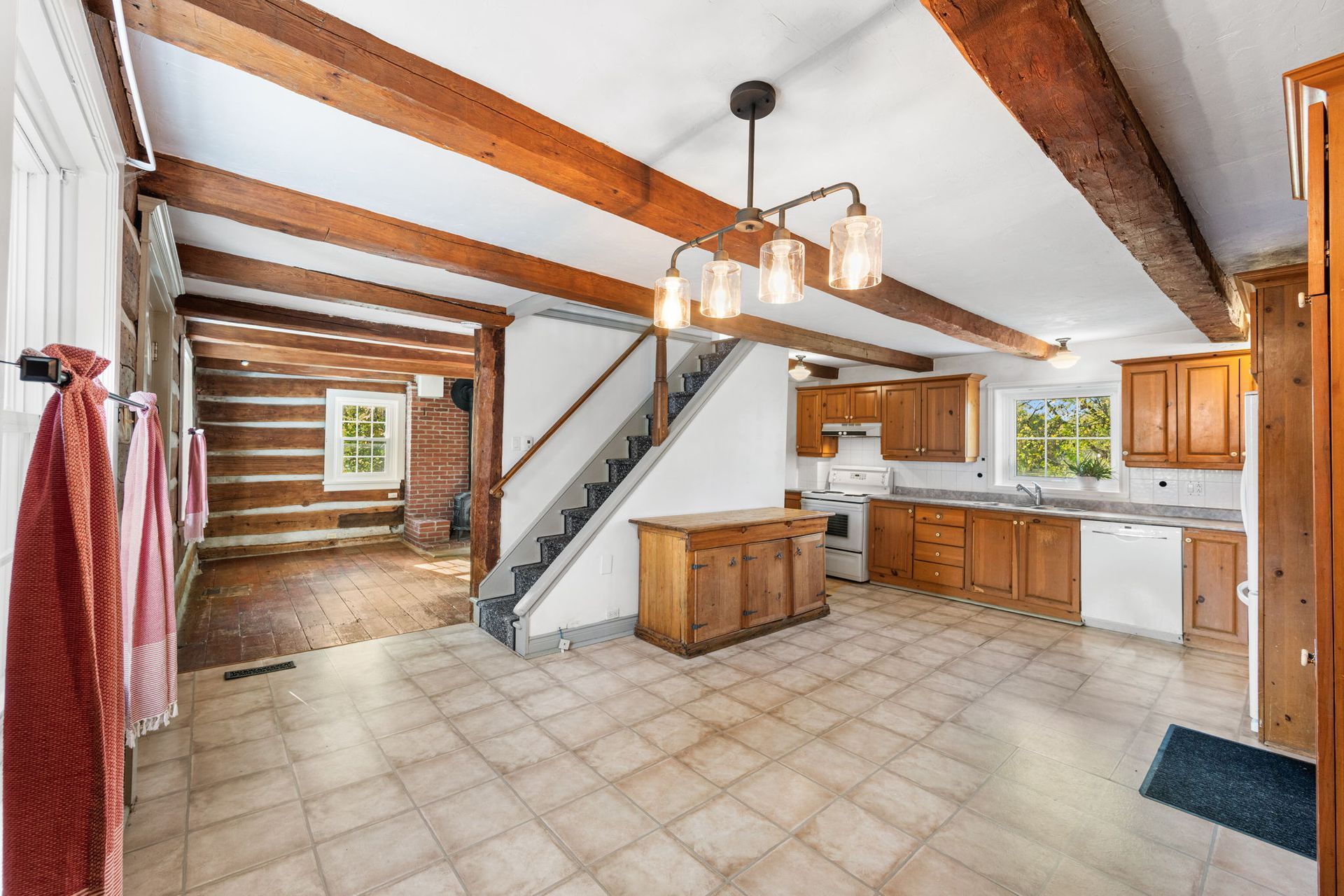Interior view of a kitchen with exposed wooden beams, staircase, and log cabin wall.