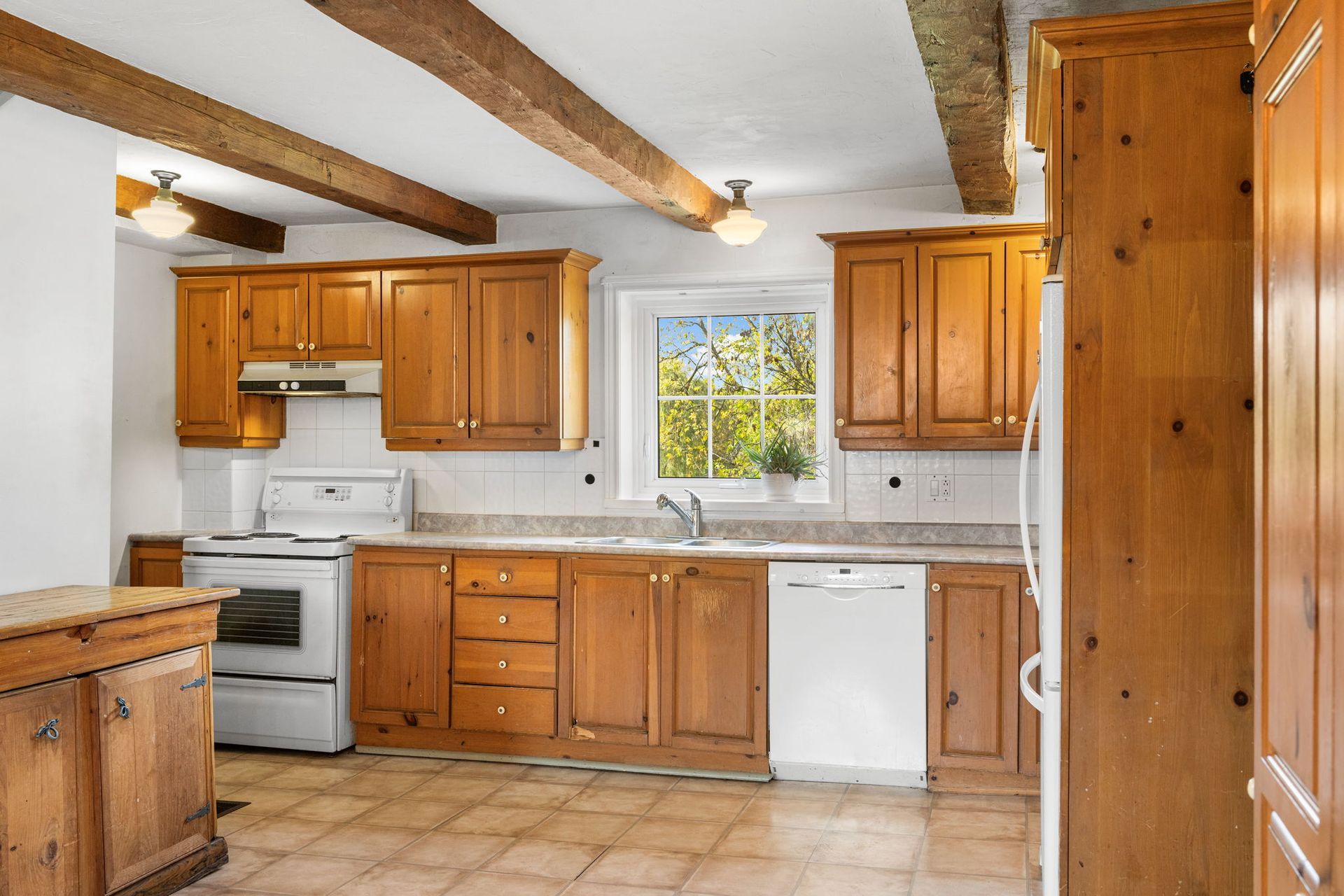 Wooden kitchen with cabinets, appliances, and a window with a view of greenery.