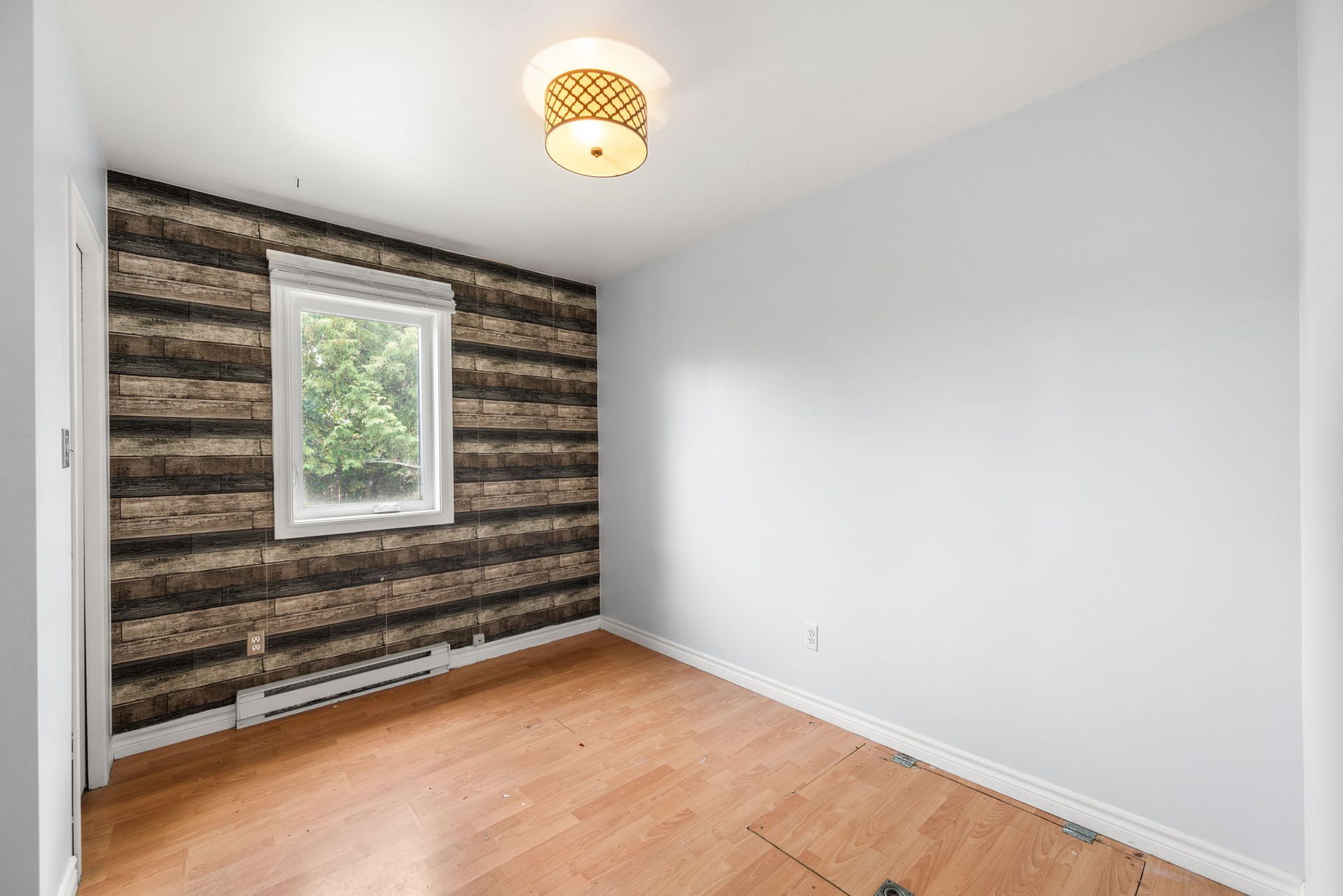Empty room with wood-look accent wall, window, and light wood floors.