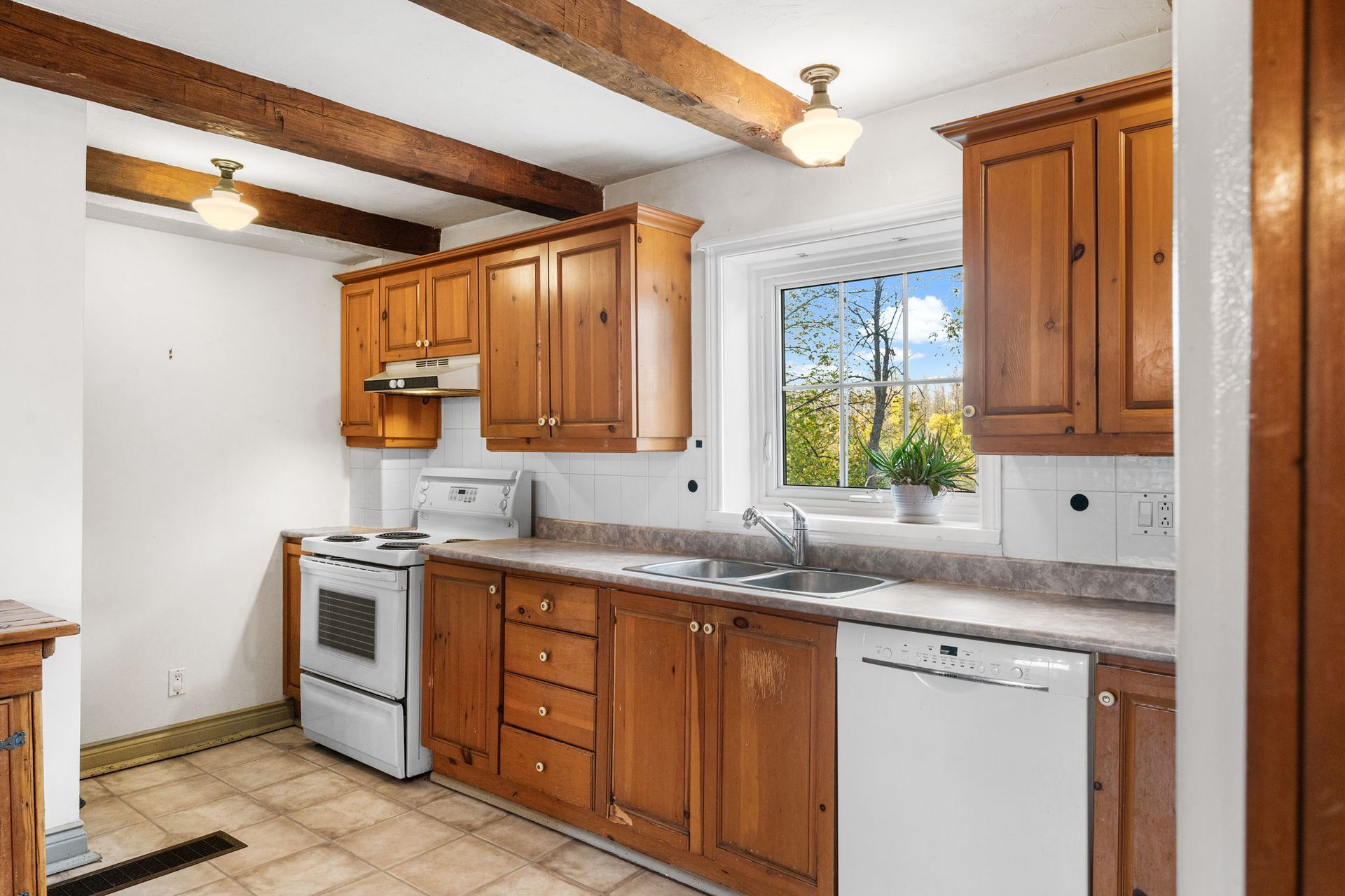Kitchen with wooden cabinets, white appliances, and tiled backsplash. Sunlight streams through a window.