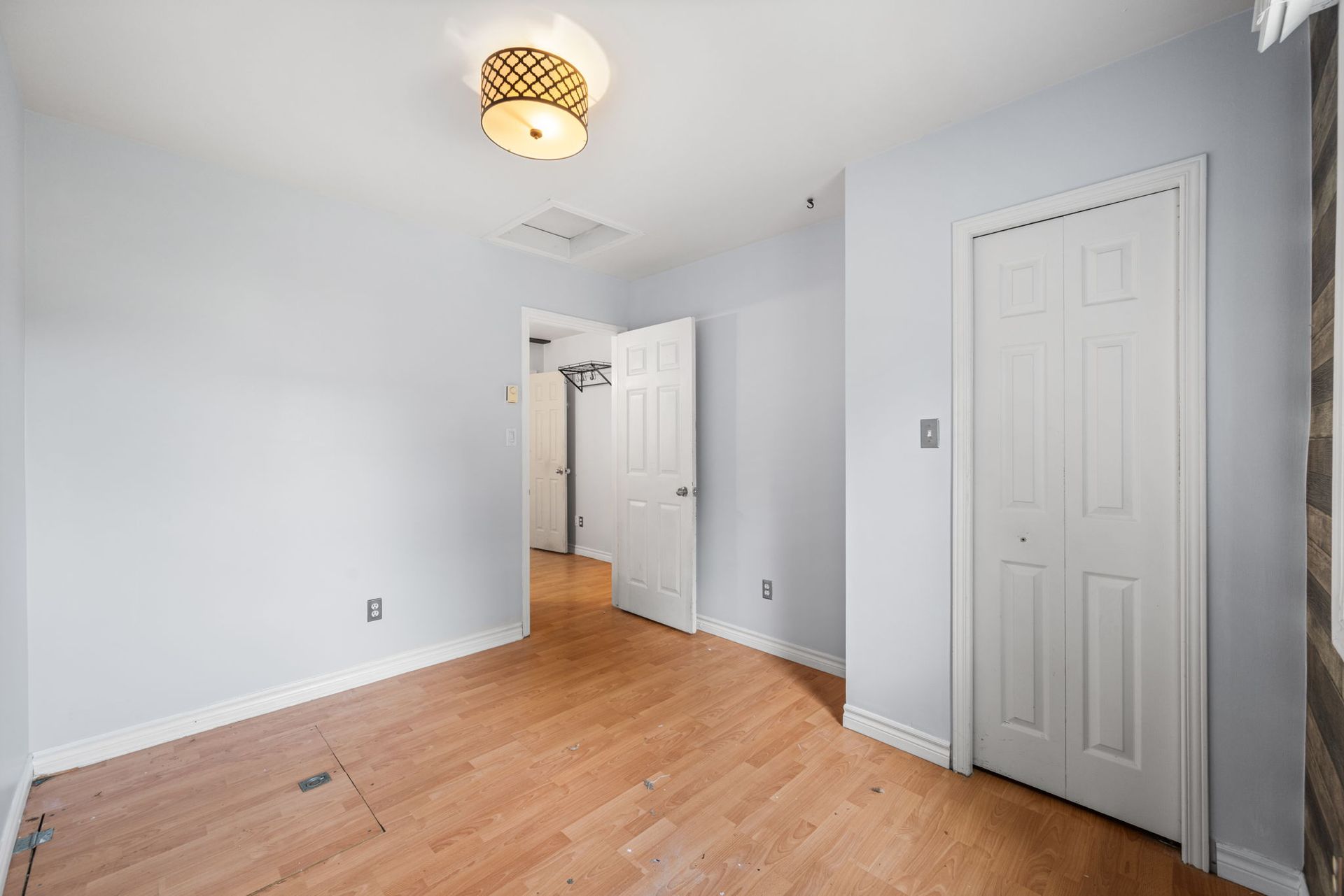 Empty bedroom with light blue walls, wood floor, and a closed white door.