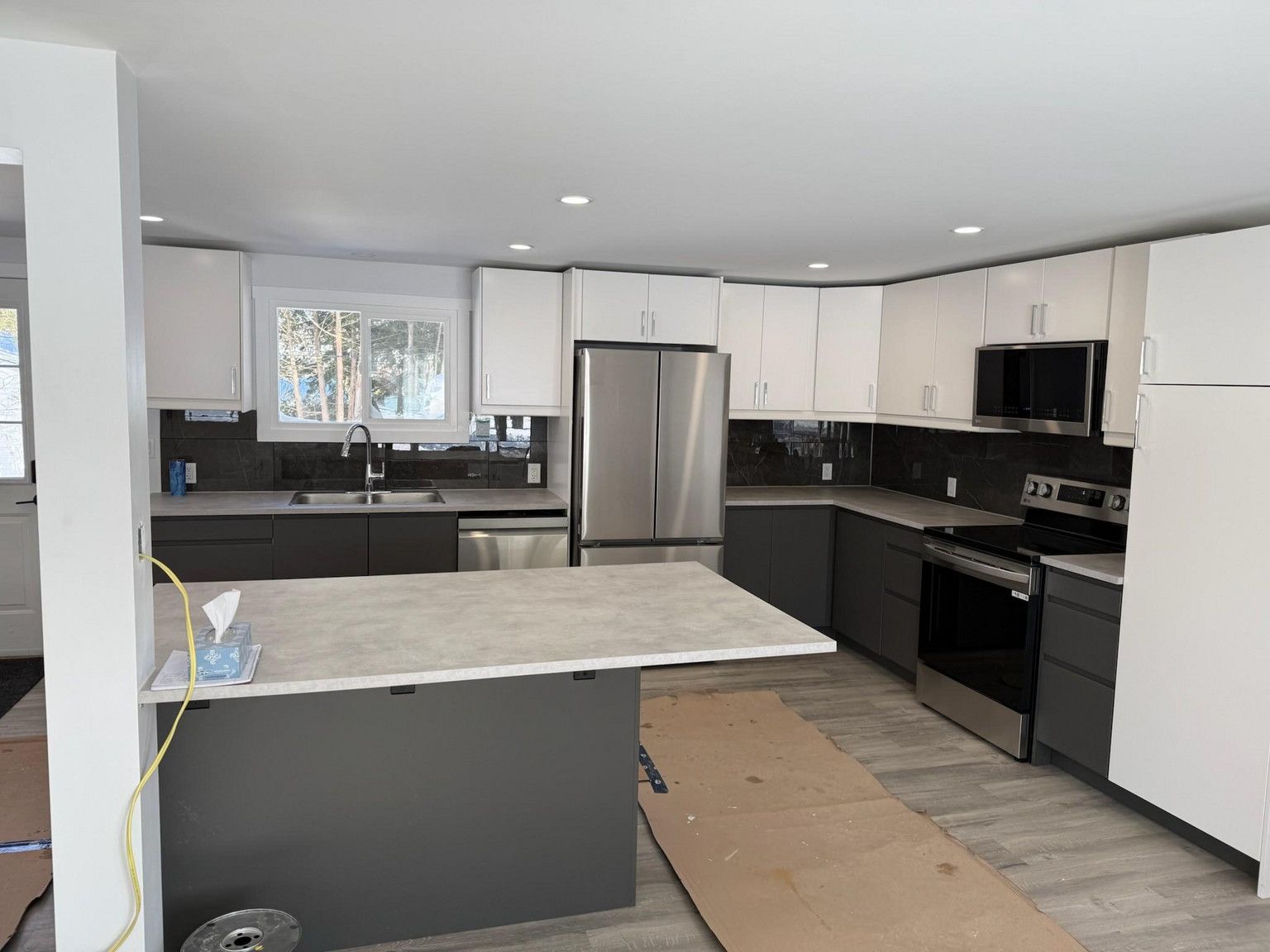 A modern kitchen with two-tone cabinetry: white upper cabinets, dark gray lower cabinets, and stainless steel appliances.