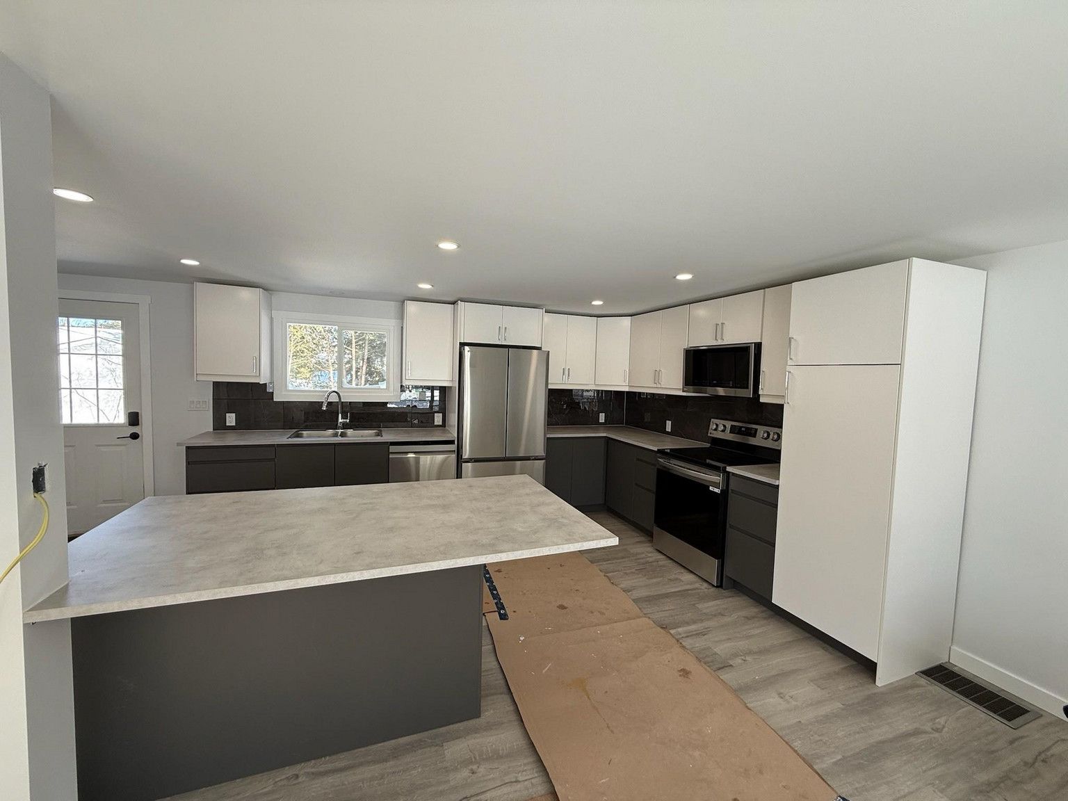 A kitchen with white upper cabinets, dark lower cabinets, a central island, stainless steel appliances, and wood floors.