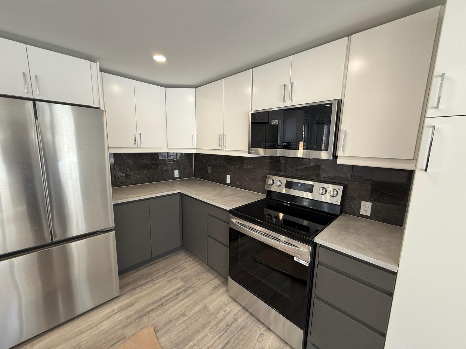 A modern kitchen featuring white upper cabinets, dark grey lower cabinets, stainless steel appliances, and dark tile walls.