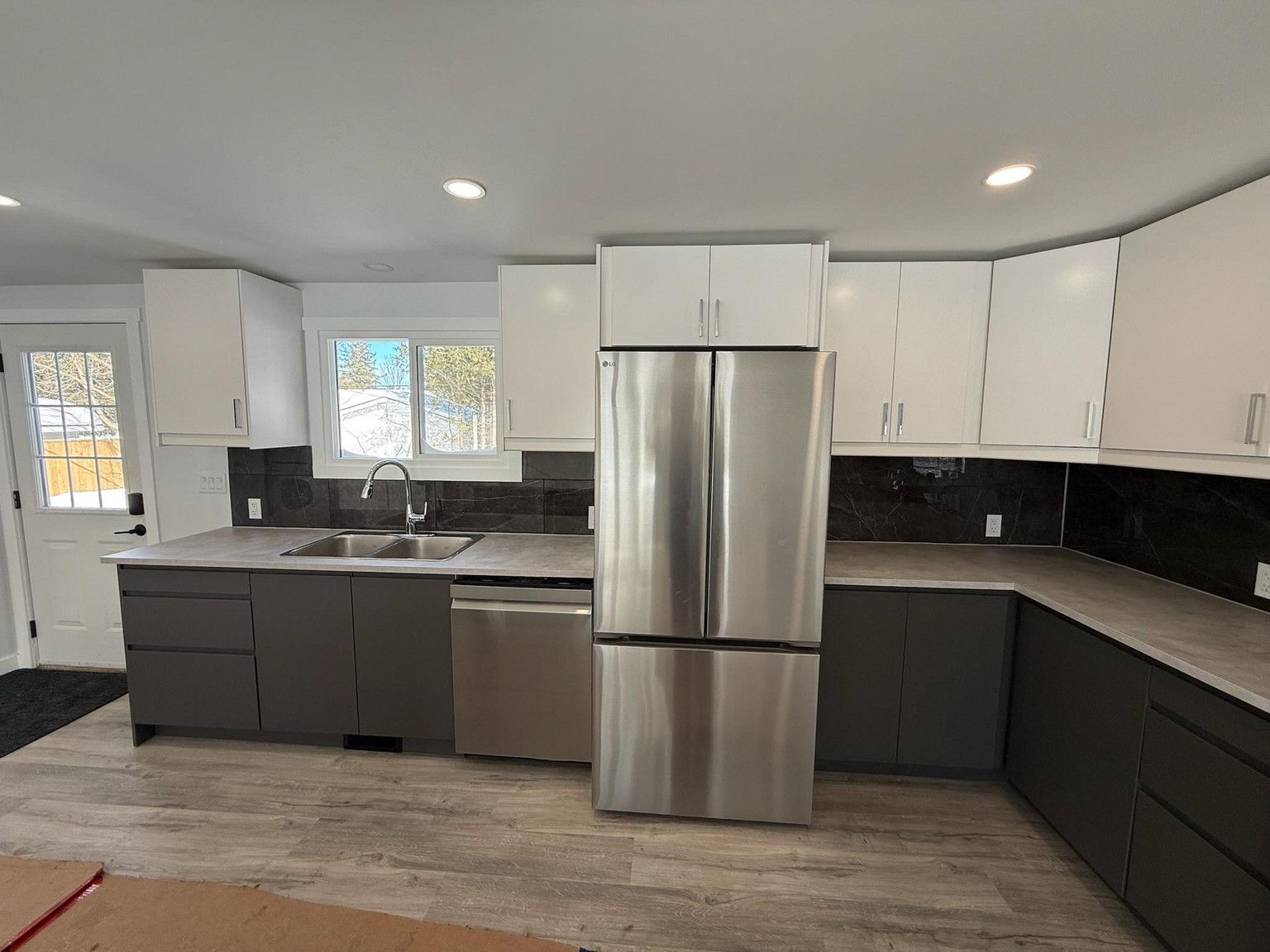 A modern kitchen featuring white upper cabinets, dark grey lower cabinets, stainless steel appliances, and wood flooring.