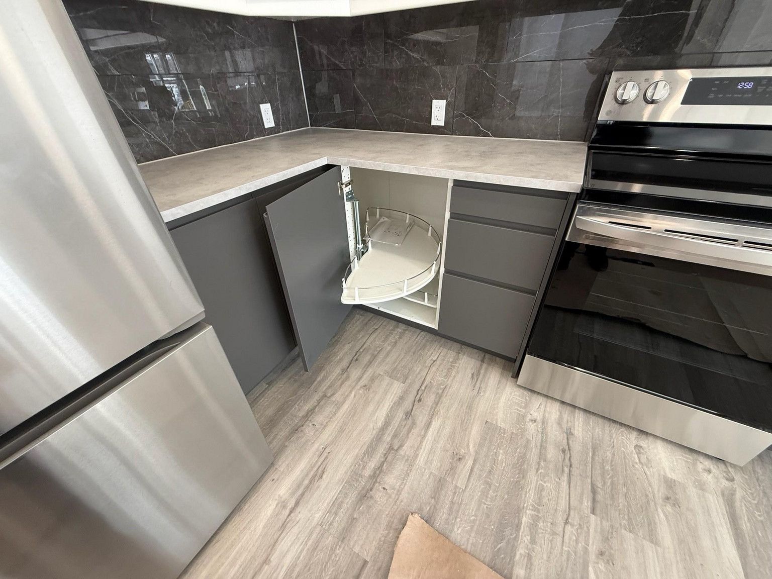 A corner kitchen cabinet with an open door revealing a white, circular pull-out storage shelf next to a stainless oven.