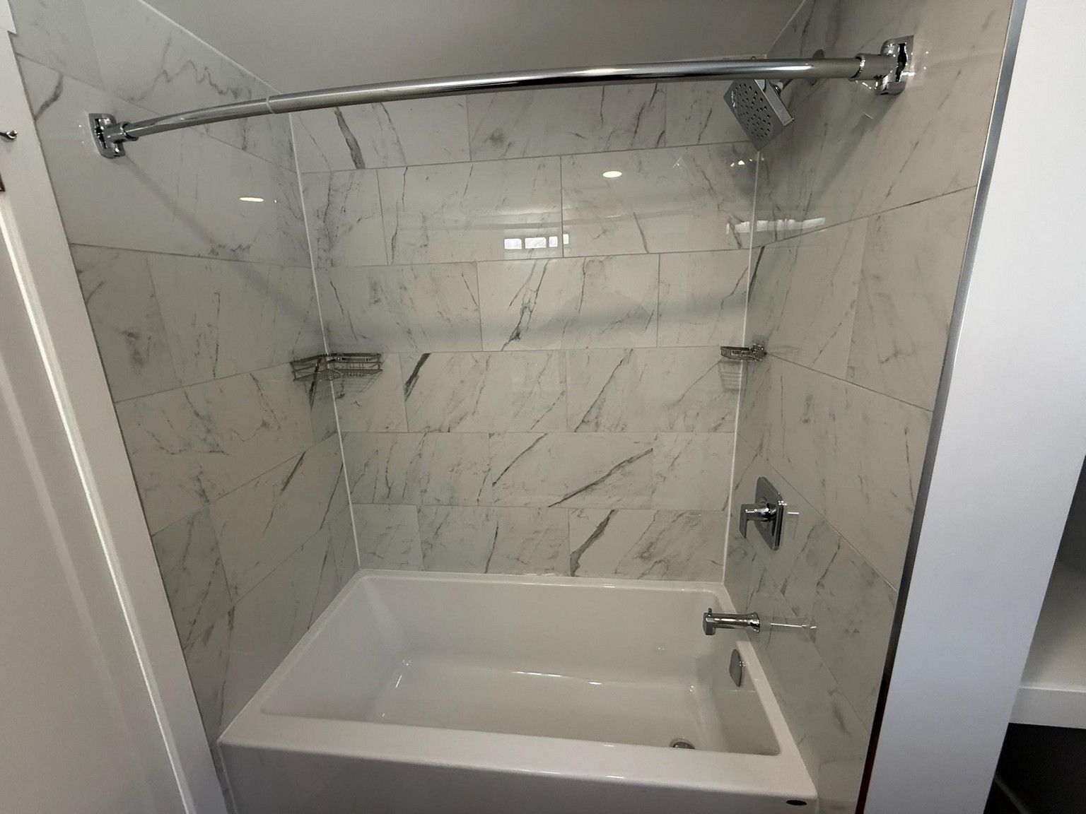 A white bathtub with a chrome faucet and showerhead, surrounded by grey and white marble-patterned tile walls.
