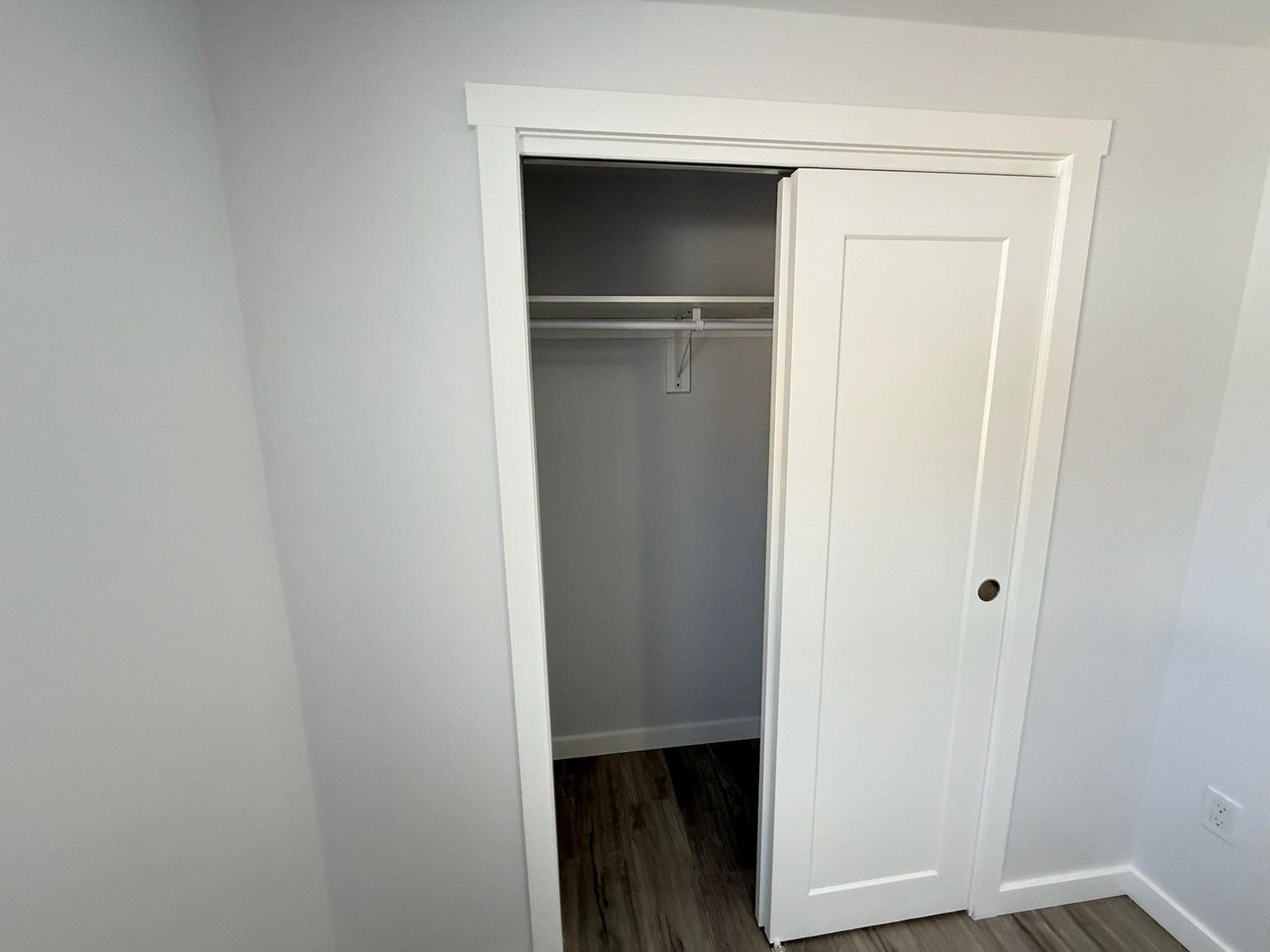 A white closet door is partially open, revealing a small, empty closet with a hanging rod against light gray walls.