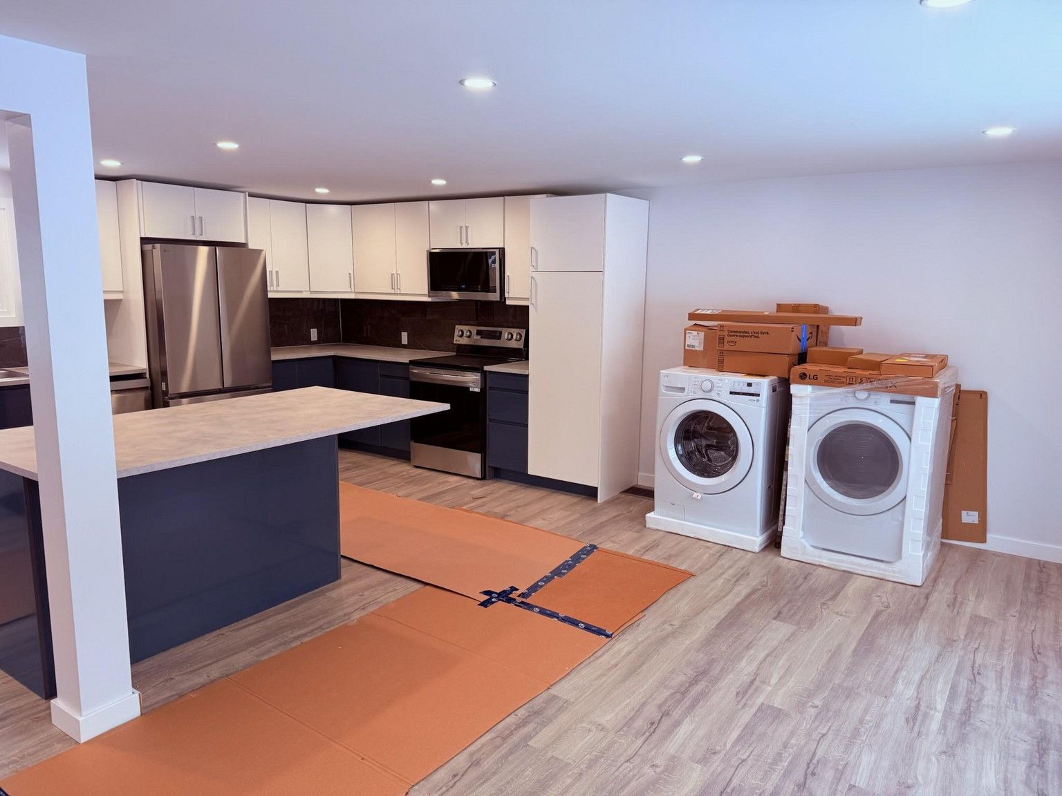 A renovated kitchen featuring blue cabinetry, a stainless steel refrigerator, and two new laundry appliances in the room.
