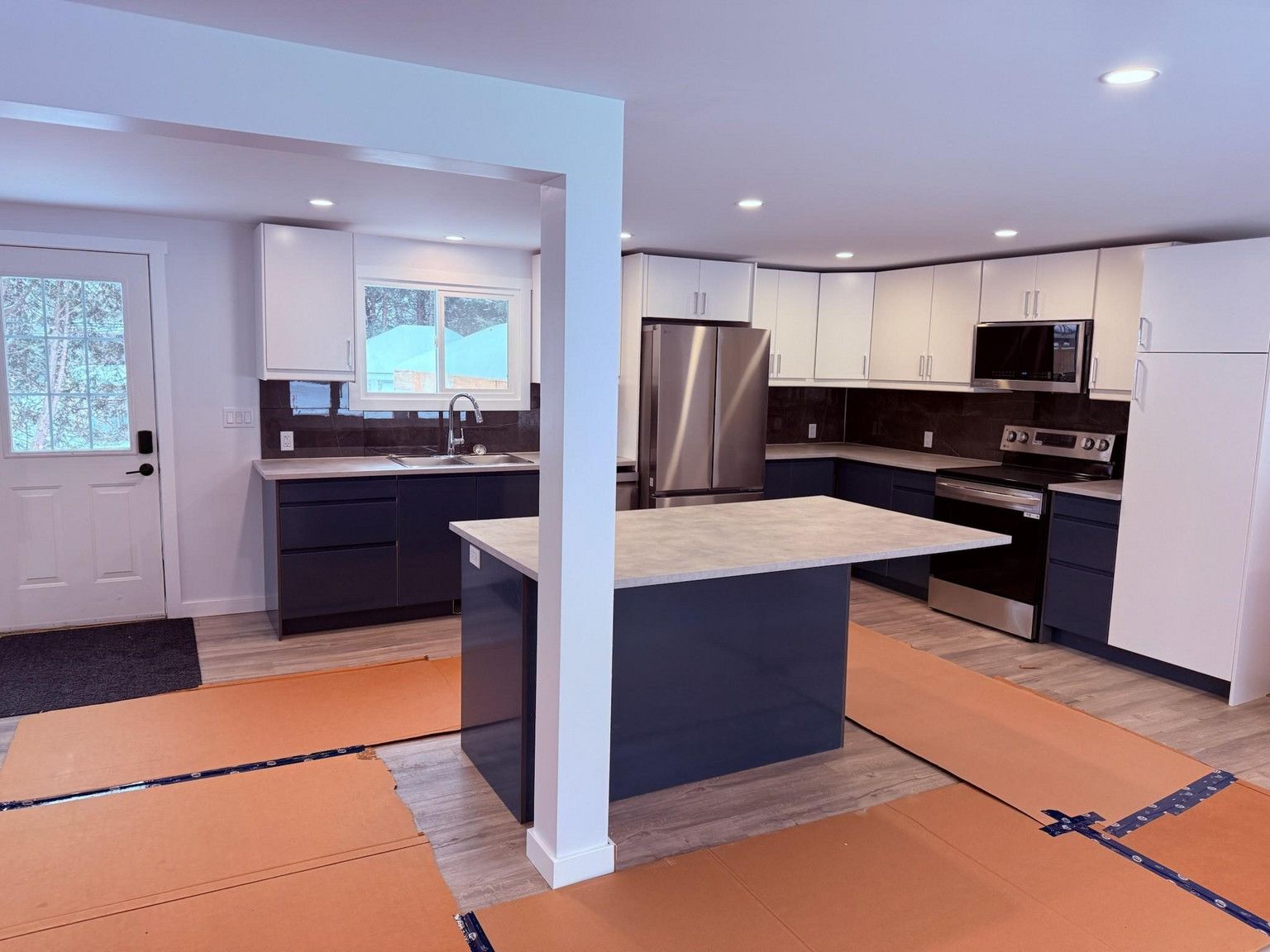A newly renovated kitchen with dark blue lower cabinets, white upper cabinets, a center island, and protective floor paper.