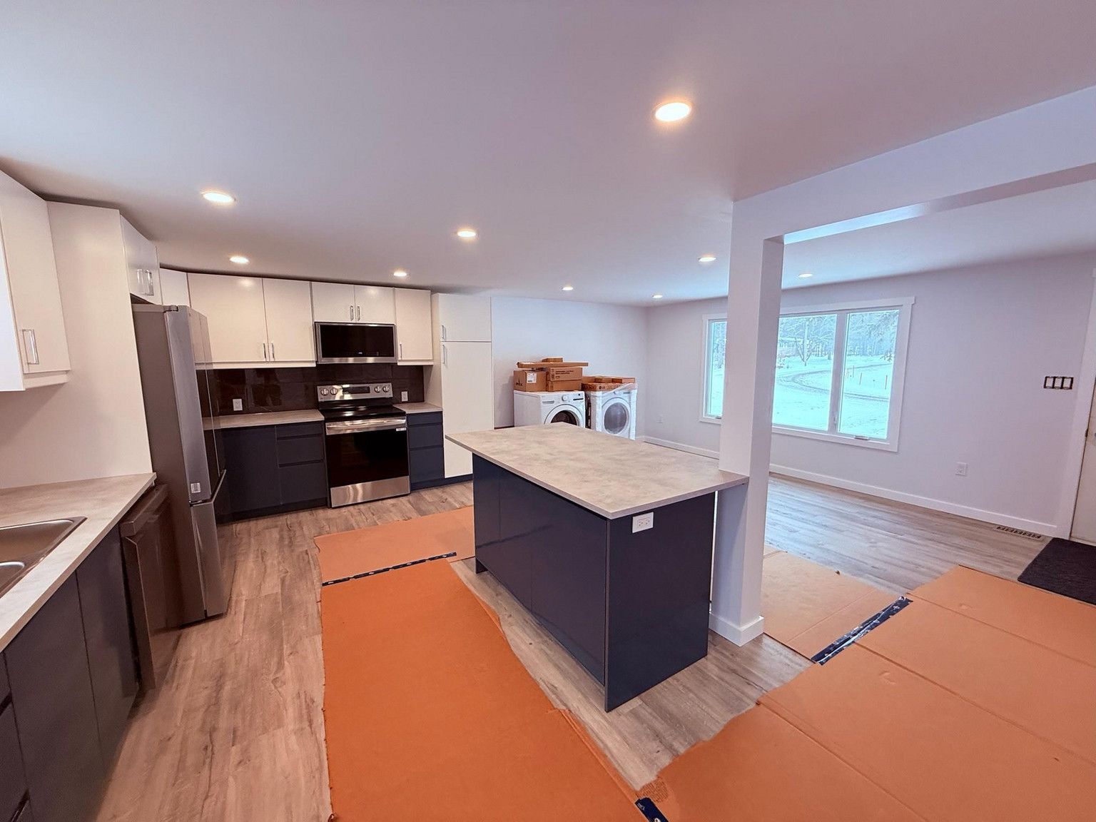A modern kitchen with dark blue lower cabinets, a central island, stainless steel appliances, and protective floor covers.