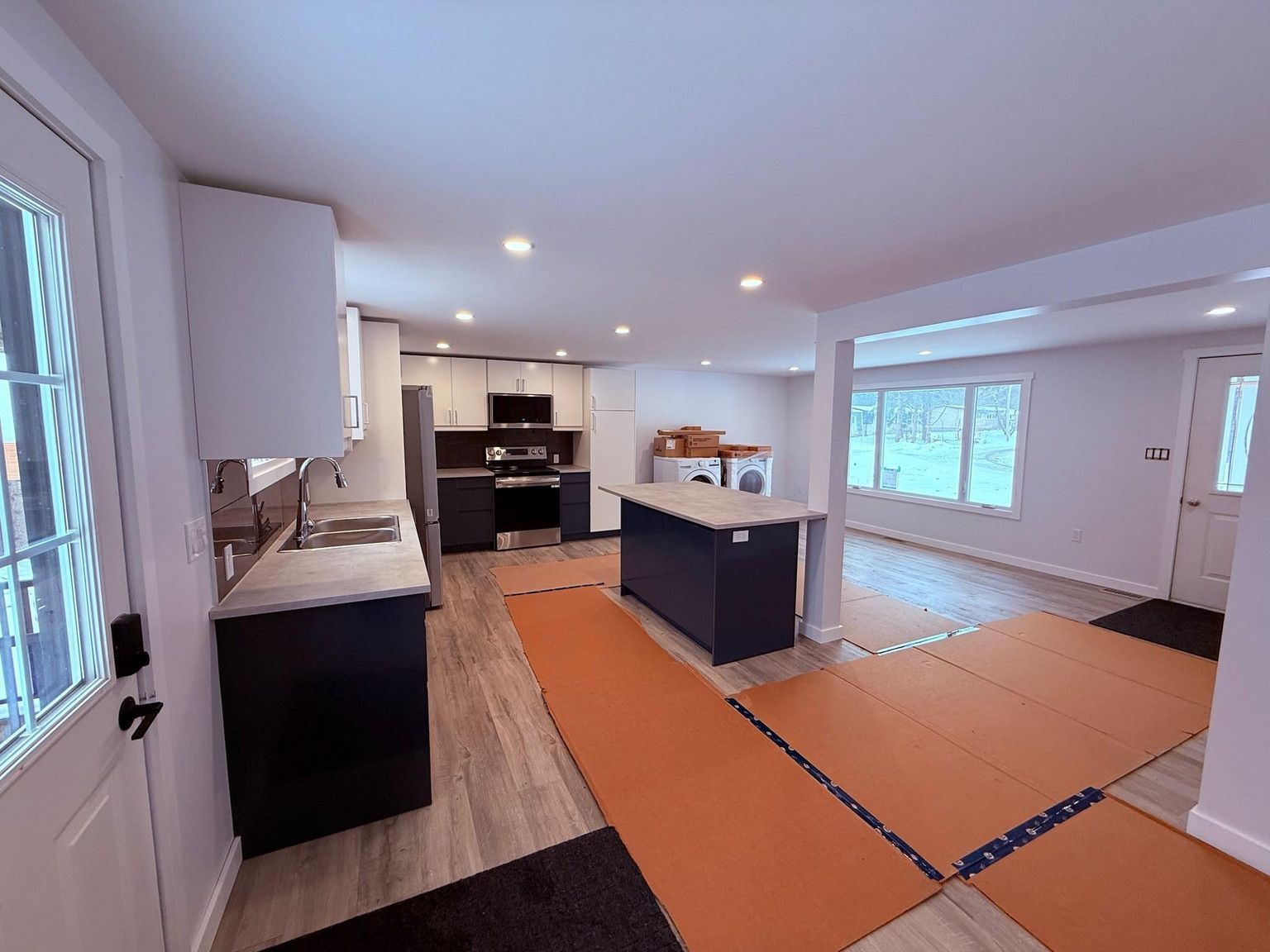 A kitchen featuring a dark blue island and cabinets, light wood-look floors, and protective floor mats in a home interior.