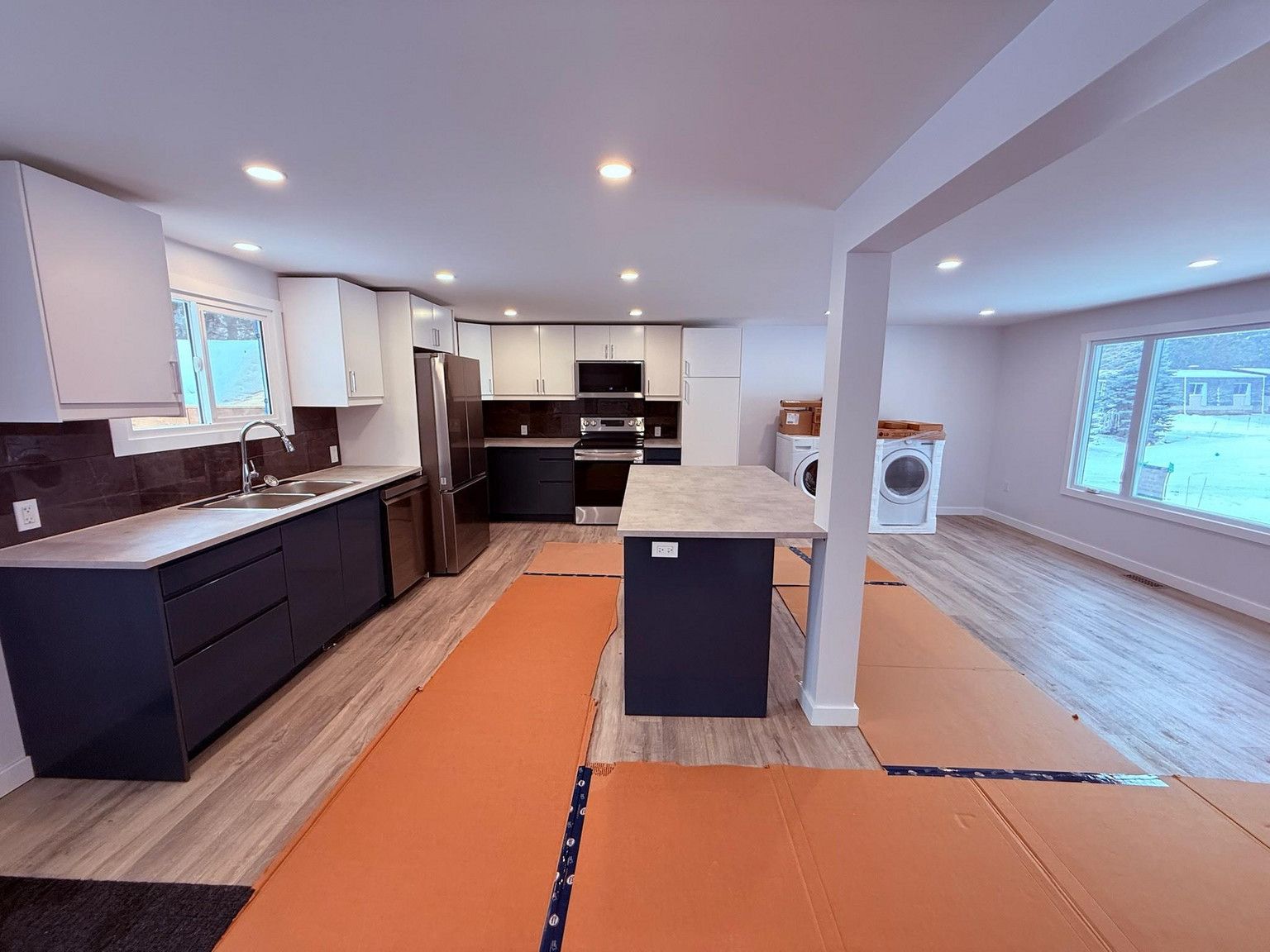 Modern kitchen with dark cabinets, a center island, and white wall cabinets, with floor protection paper in a bright home.