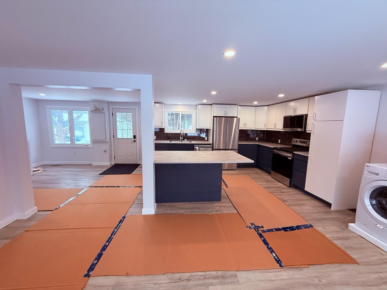 A bright, newly renovated kitchen with dark blue cabinets, a central island, and protective paper covering the floors.