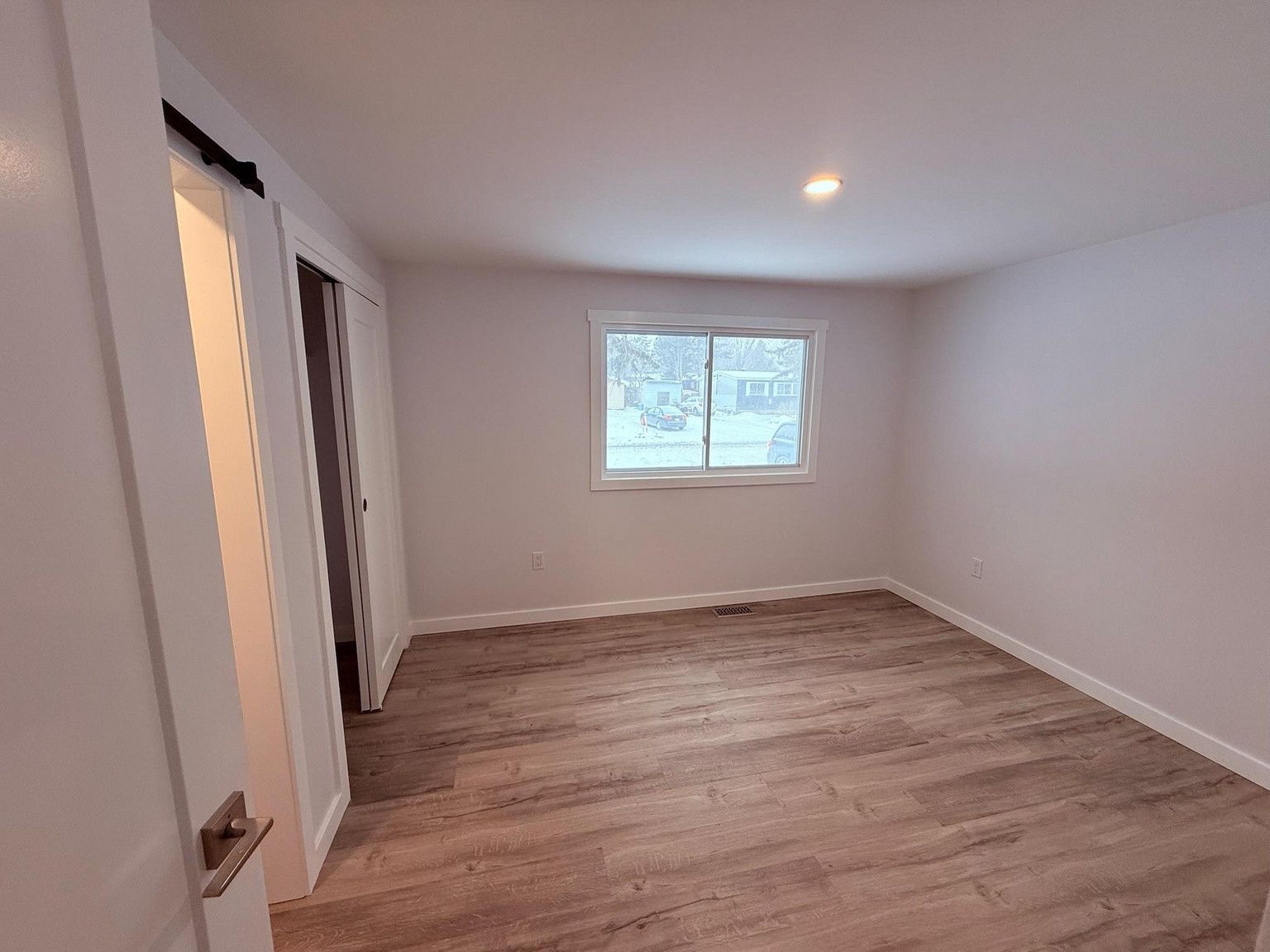 An empty room with light gray walls, light wood-look flooring, and a window centered on the far wall.