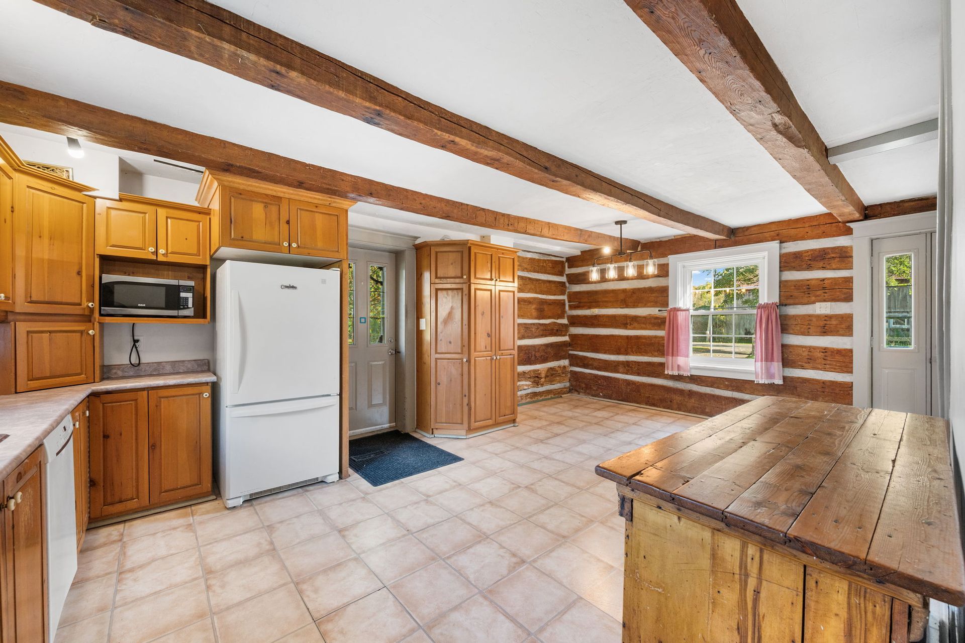 Kitchen interior with wooden beams, cabinets, and a rustic table, next to a log cabin wall.