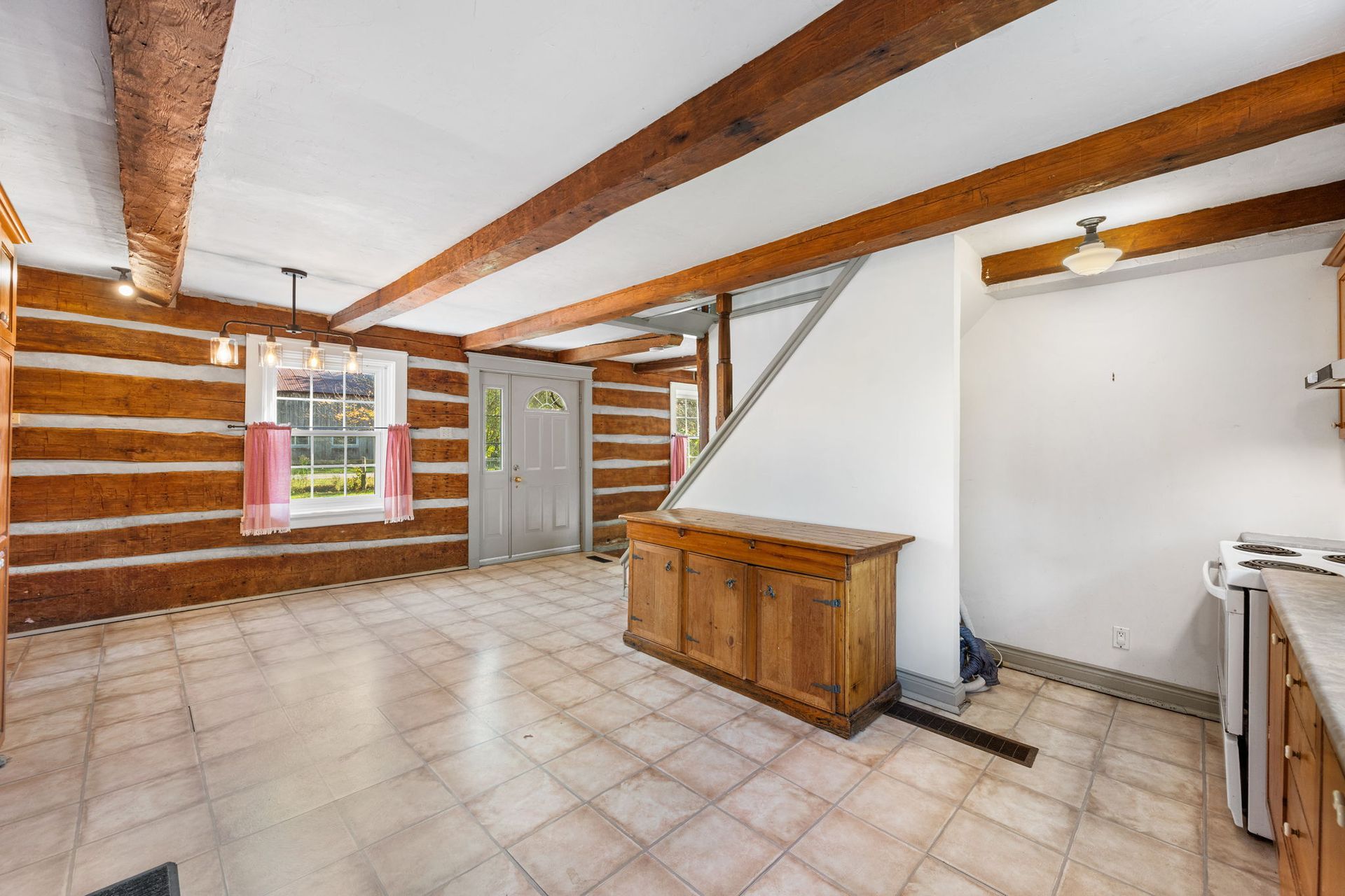Interior of a room with log walls, wood beams, tiled floor, and a wooden cabinet.