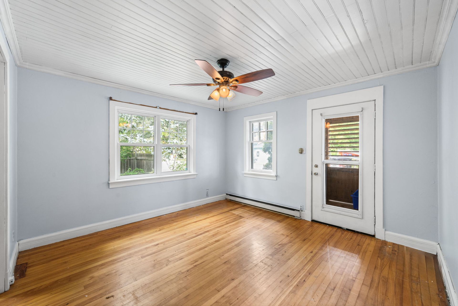 Empty room with wood floors, light blue walls, white trim, and ceiling fan.