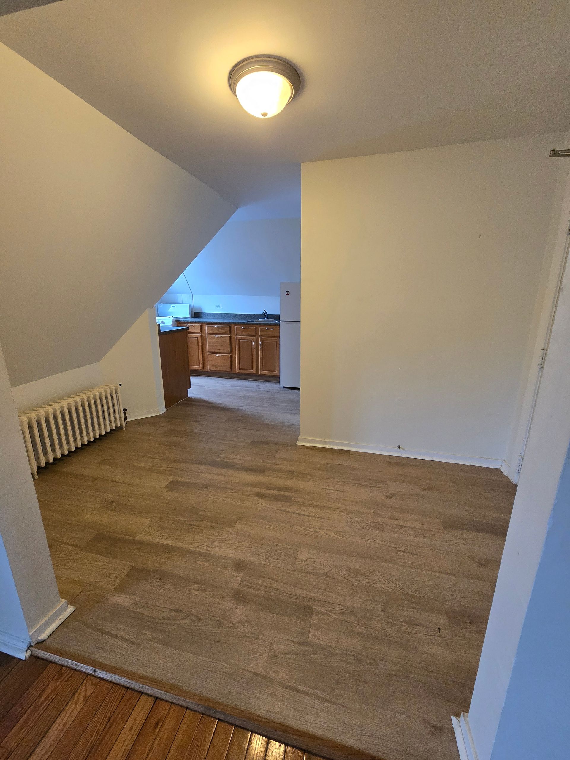 An empty room with hardwood floors and a kitchen in the background.