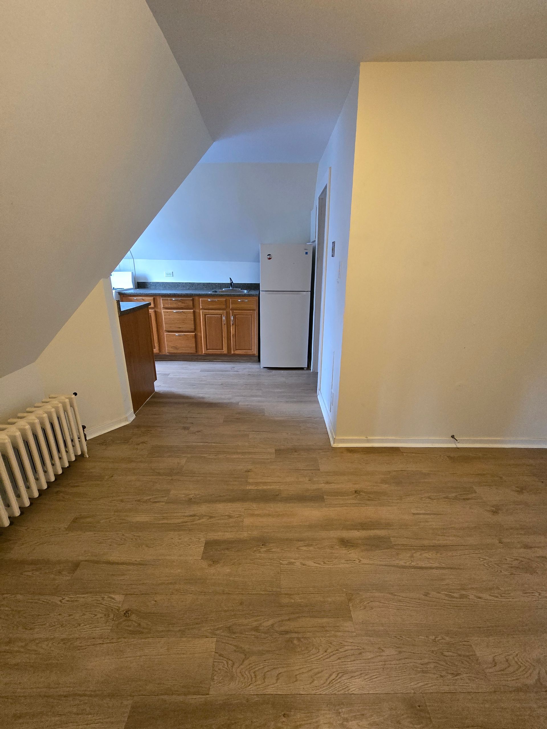 An empty room with hardwood floors and a refrigerator in a kitchen.