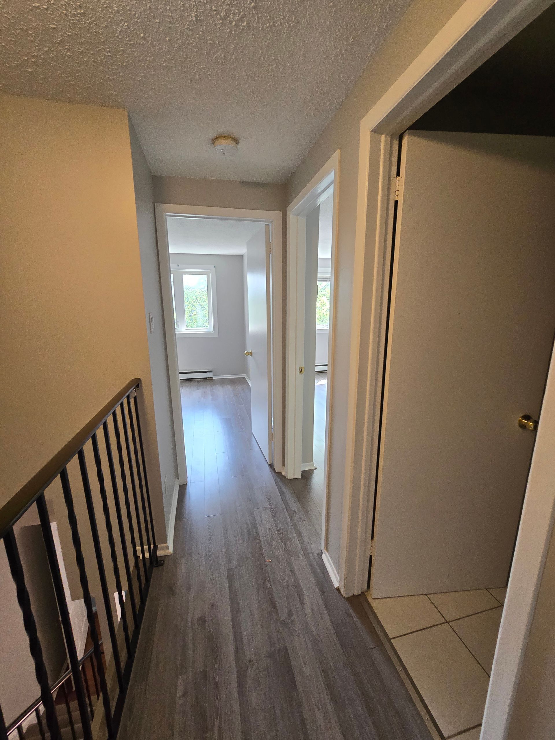 A hallway with hardwood floors and a railing leading to a living room.