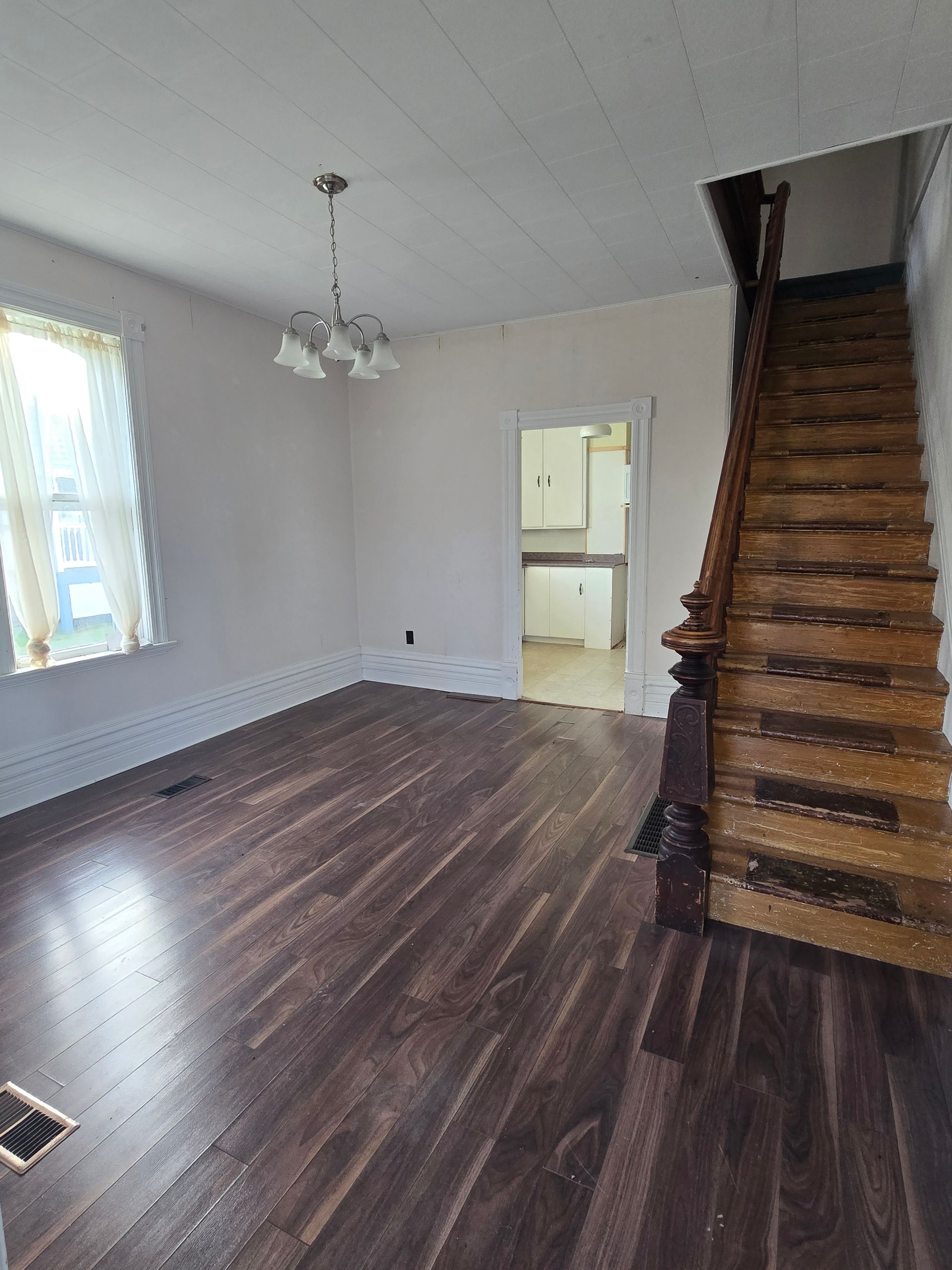 Living room with dark wood floor, stairs, and doorway to kitchen.