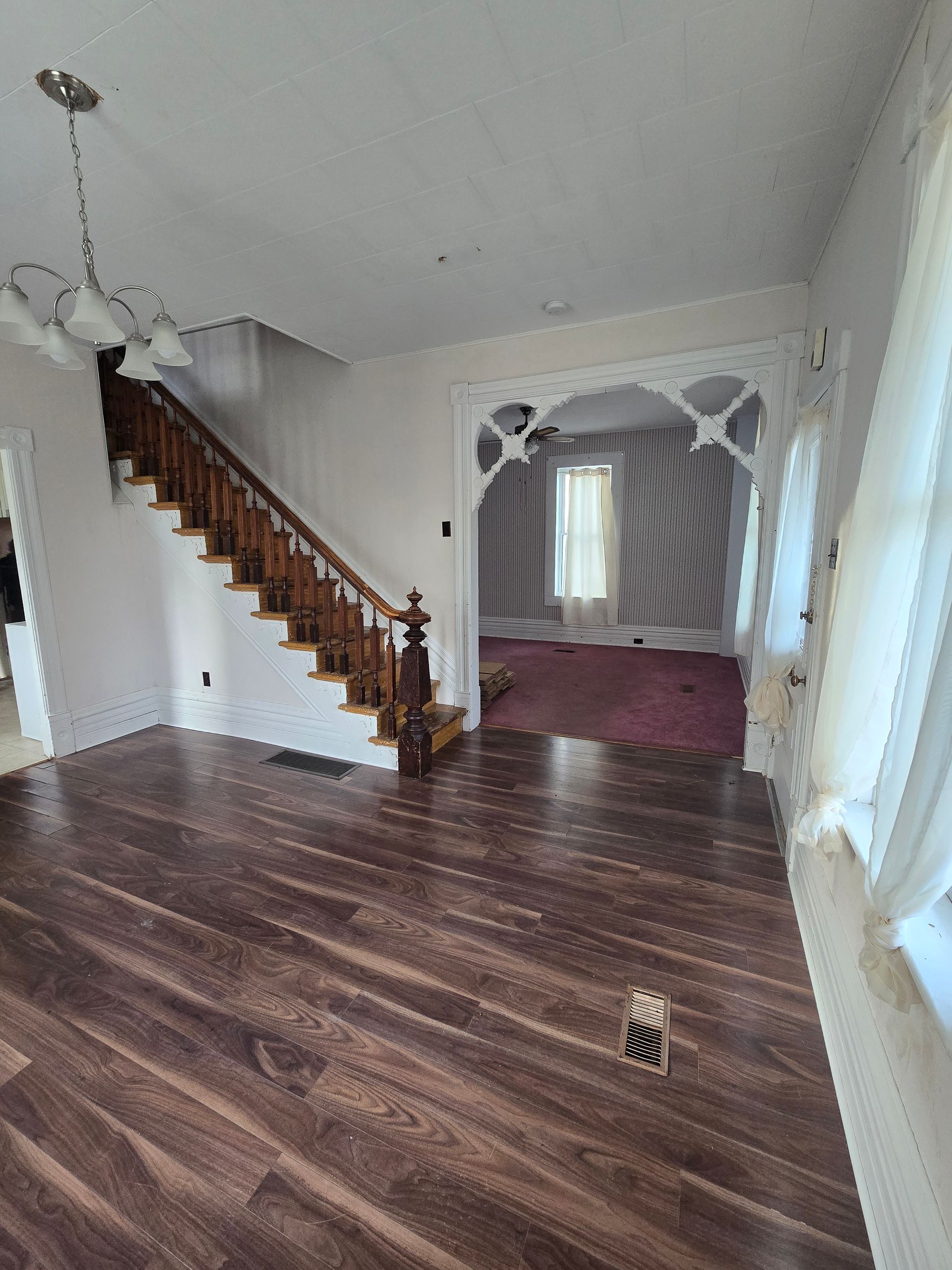 Interior view of a house with a staircase, decorative archway, and wood flooring.