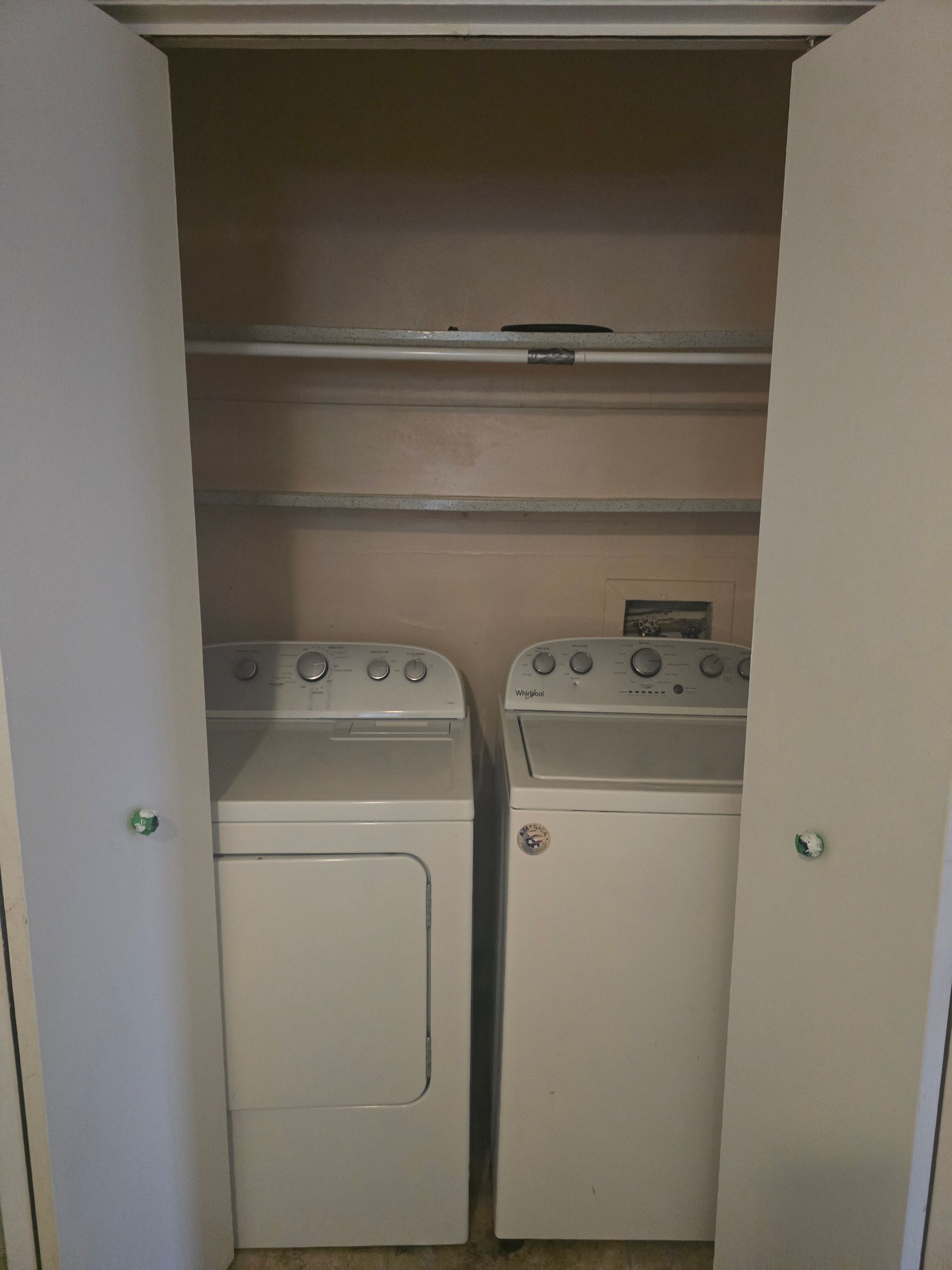 Laundry machines, a dryer and washing machine, sit in a closet. The white appliances are surrounded by the closet walls and doors.