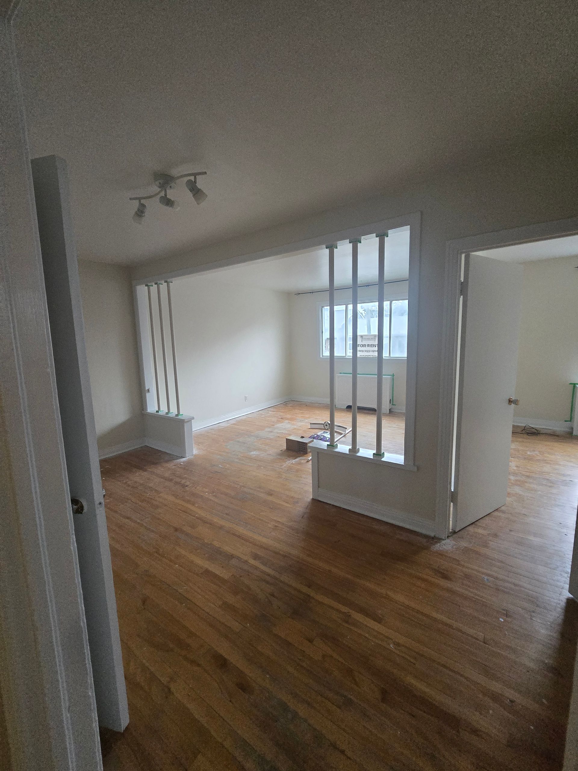 Interior view of a room with hardwood floors and a decorative white partition with vertical slats. A window is visible in the background.