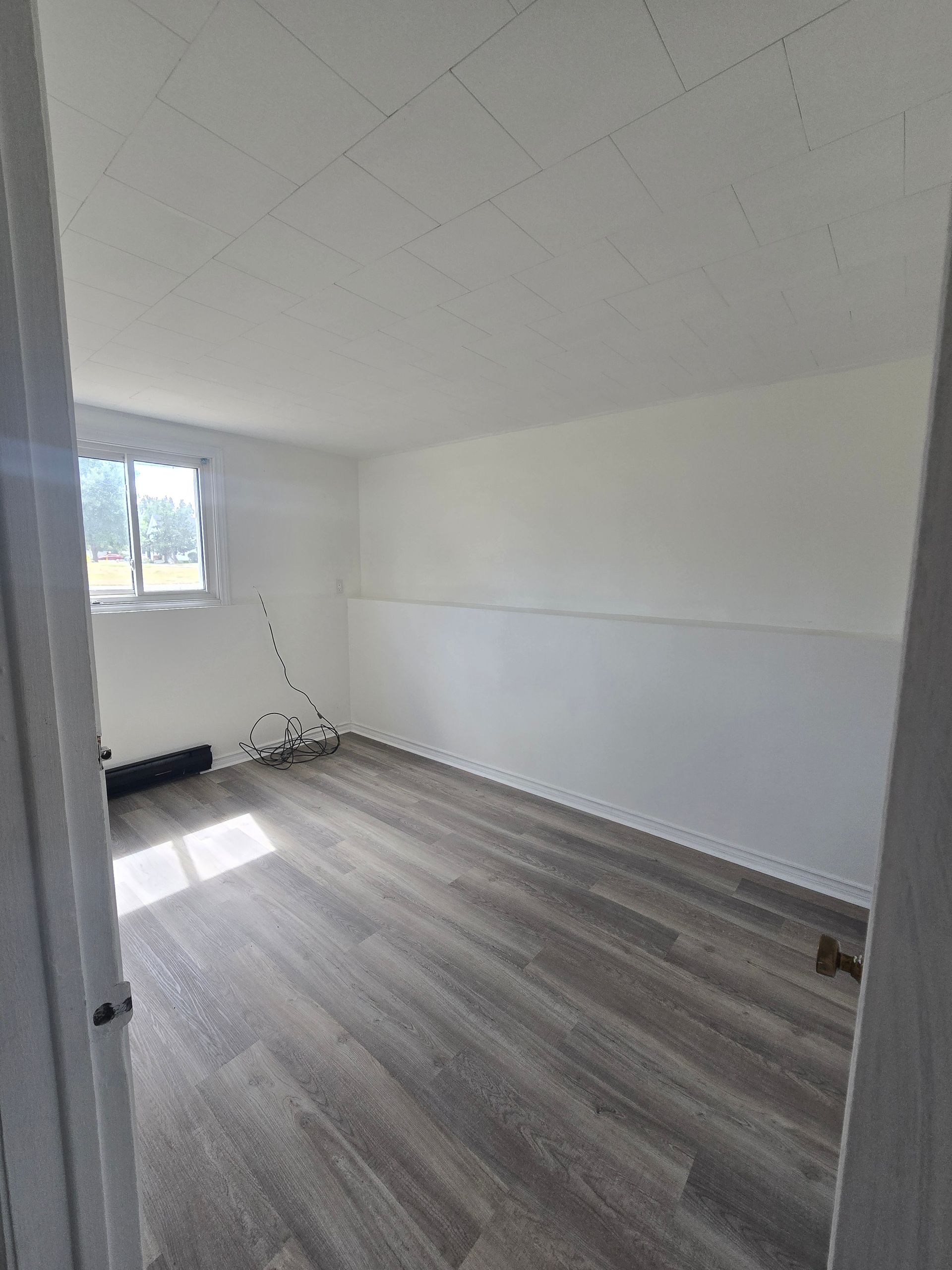 Empty room with gray wood-look flooring, white walls, and a small window.