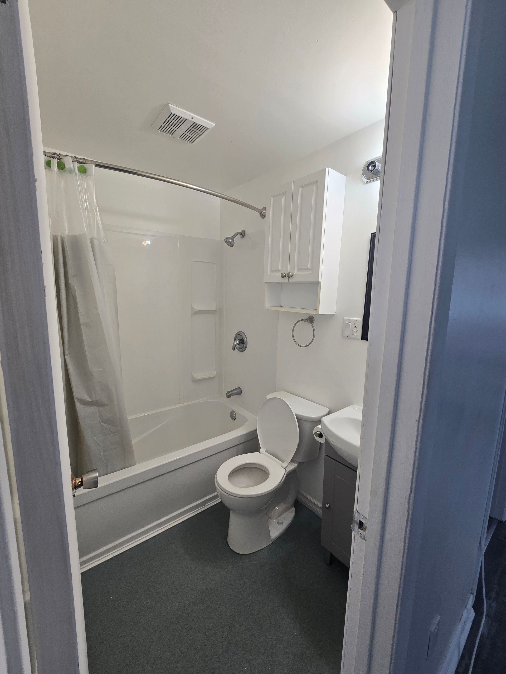 Bathroom interior with a tub, toilet, sink, and storage cabinet; white fixtures, gray floor.