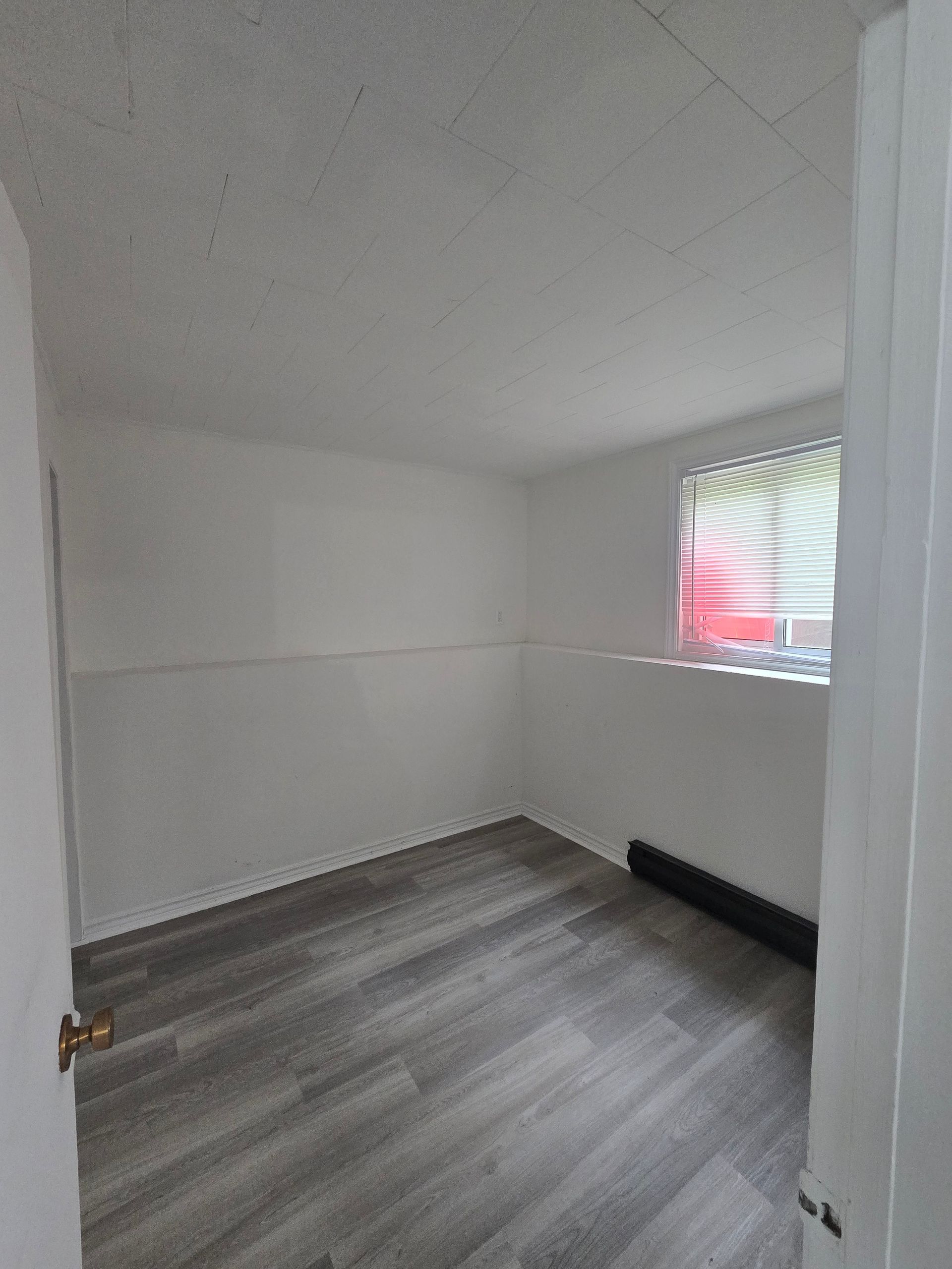 Empty room with white walls, wood-look flooring, and a small window with blinds.