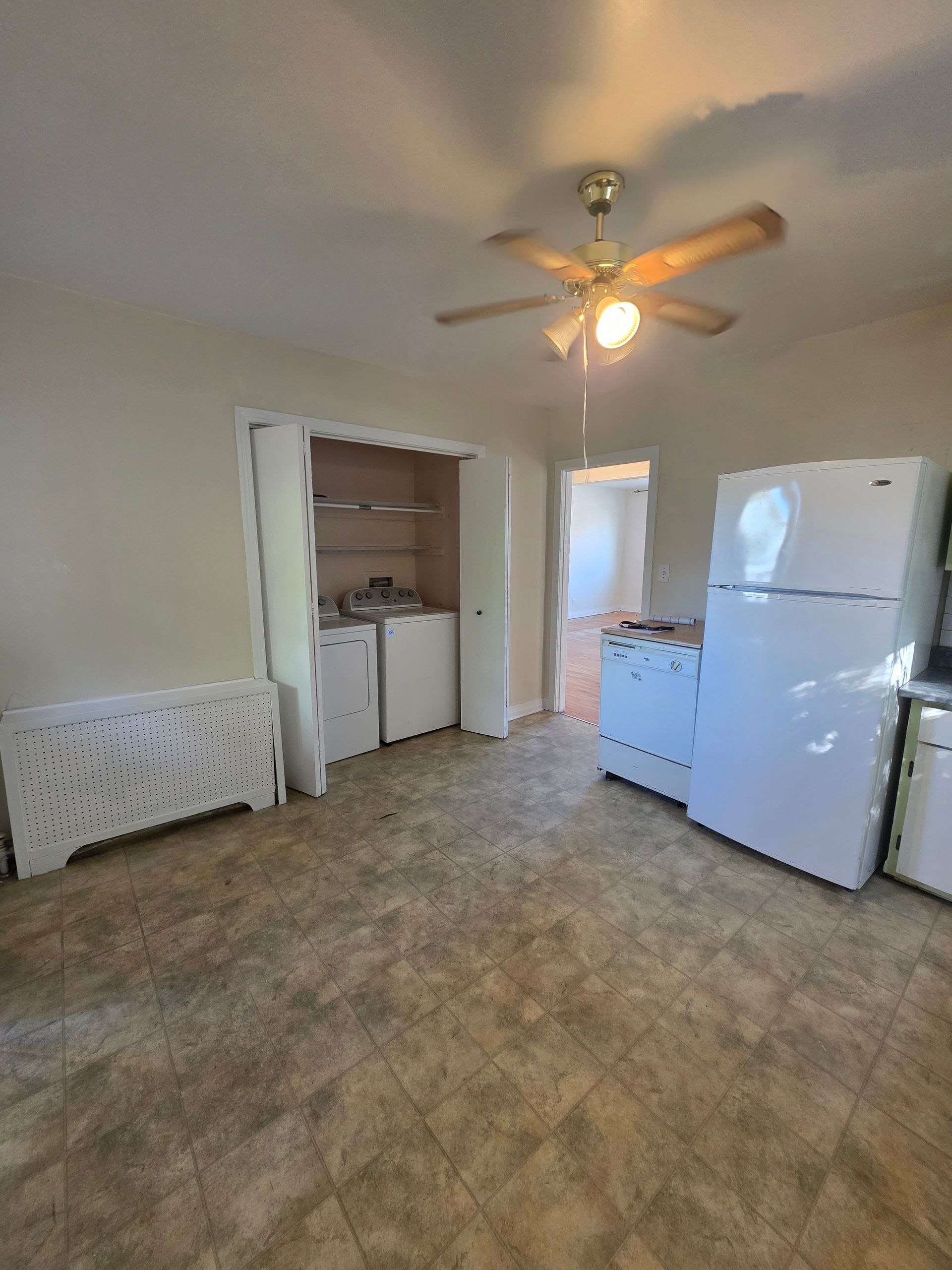 Empty room with appliances. White refrigerator and cabinets, open closet, ceiling fan. Beige flooring.