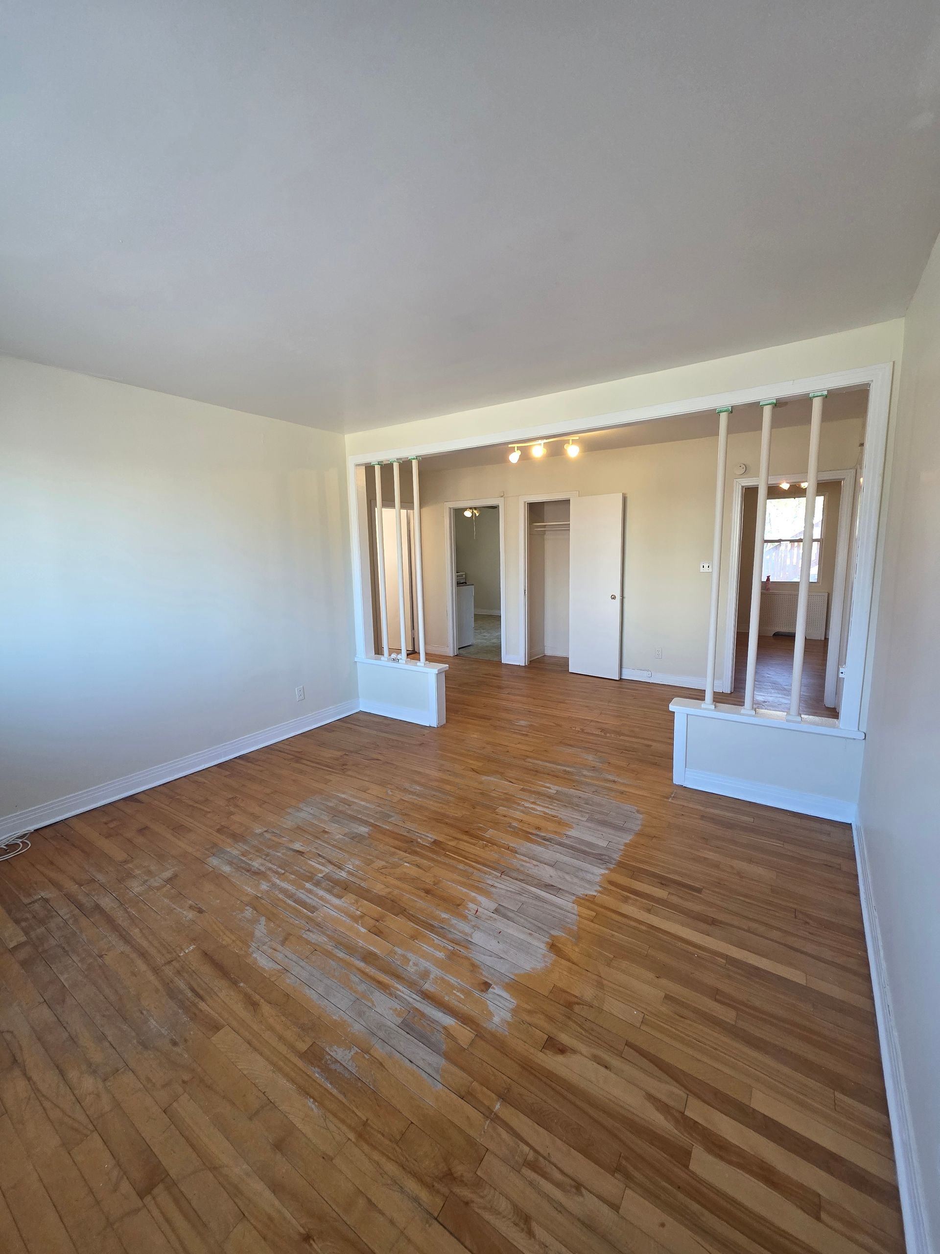 Empty living room with light-colored hardwood floors and a partial wall with vertical openings.