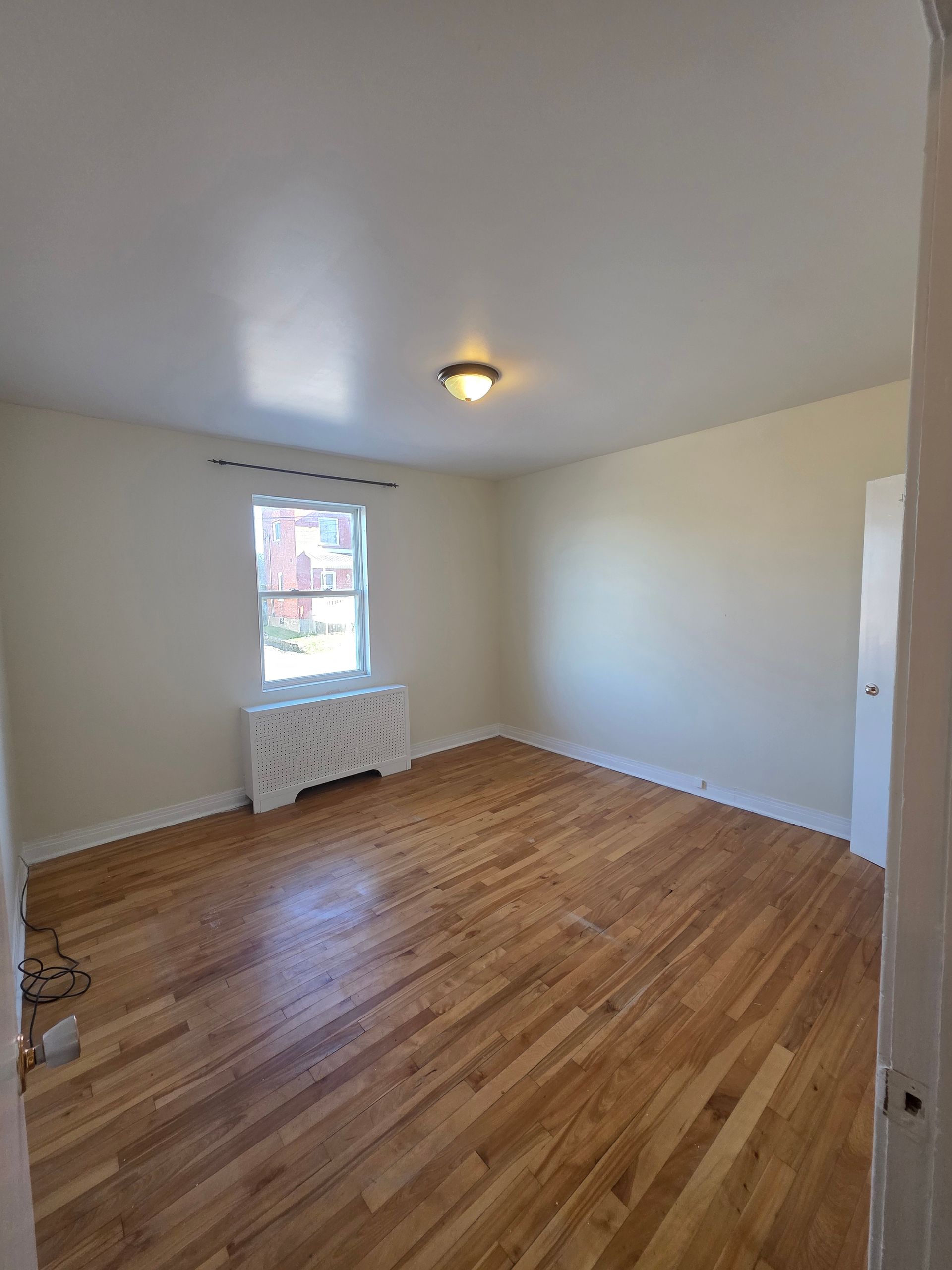 Empty room with hardwood floors, a window, and a radiator.
