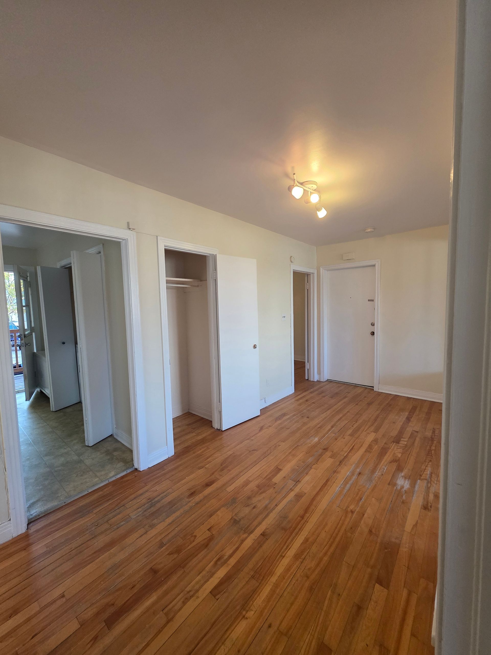 Empty room with hardwood floors, white walls, and open doorways to other rooms.