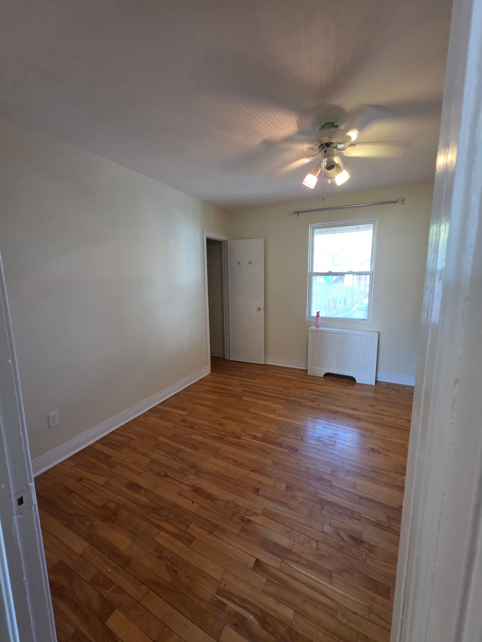 Empty room with hardwood floors, white walls, and a window.