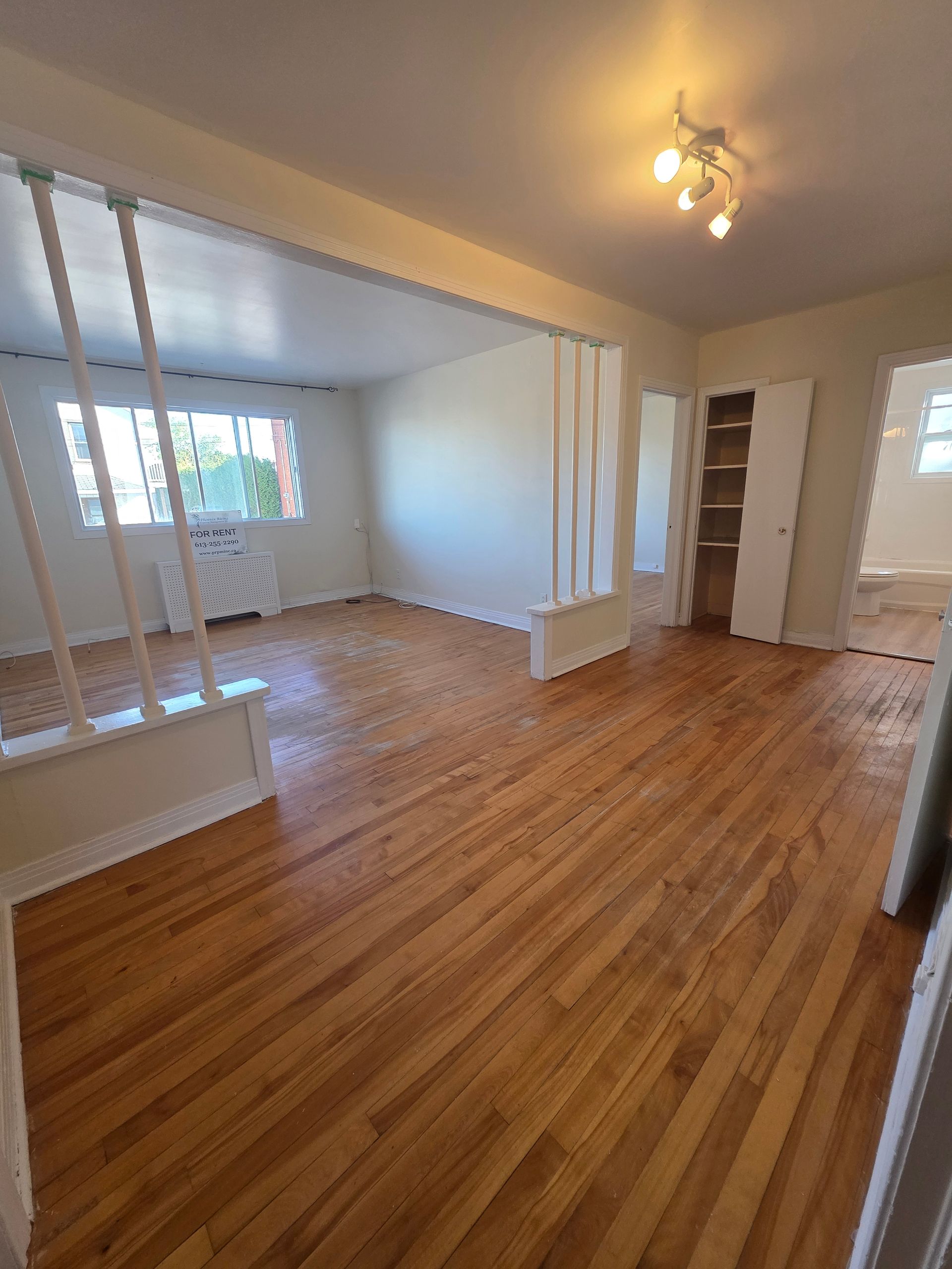 Wooden-floored interior with white walls, built-in shelving, and a doorway leading to another room.