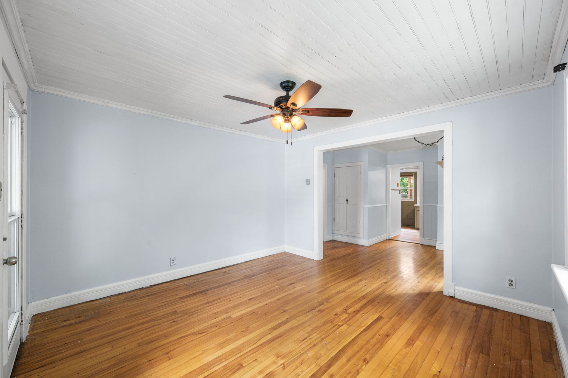 Empty living room with hardwood floors, blue walls, white trim, and a ceiling fan.
