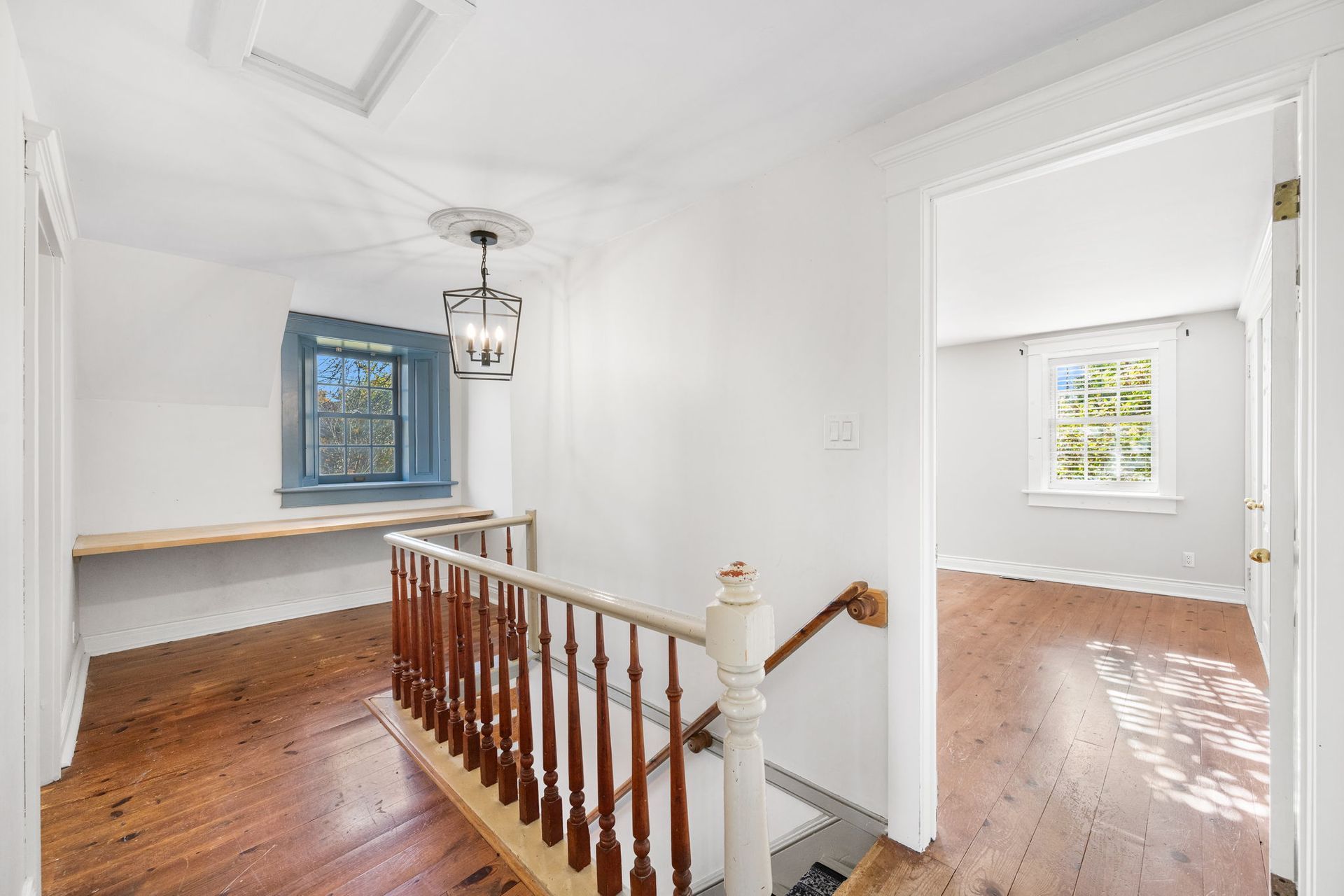 Hallway with wood floors, railing, window, and doorway to another room.