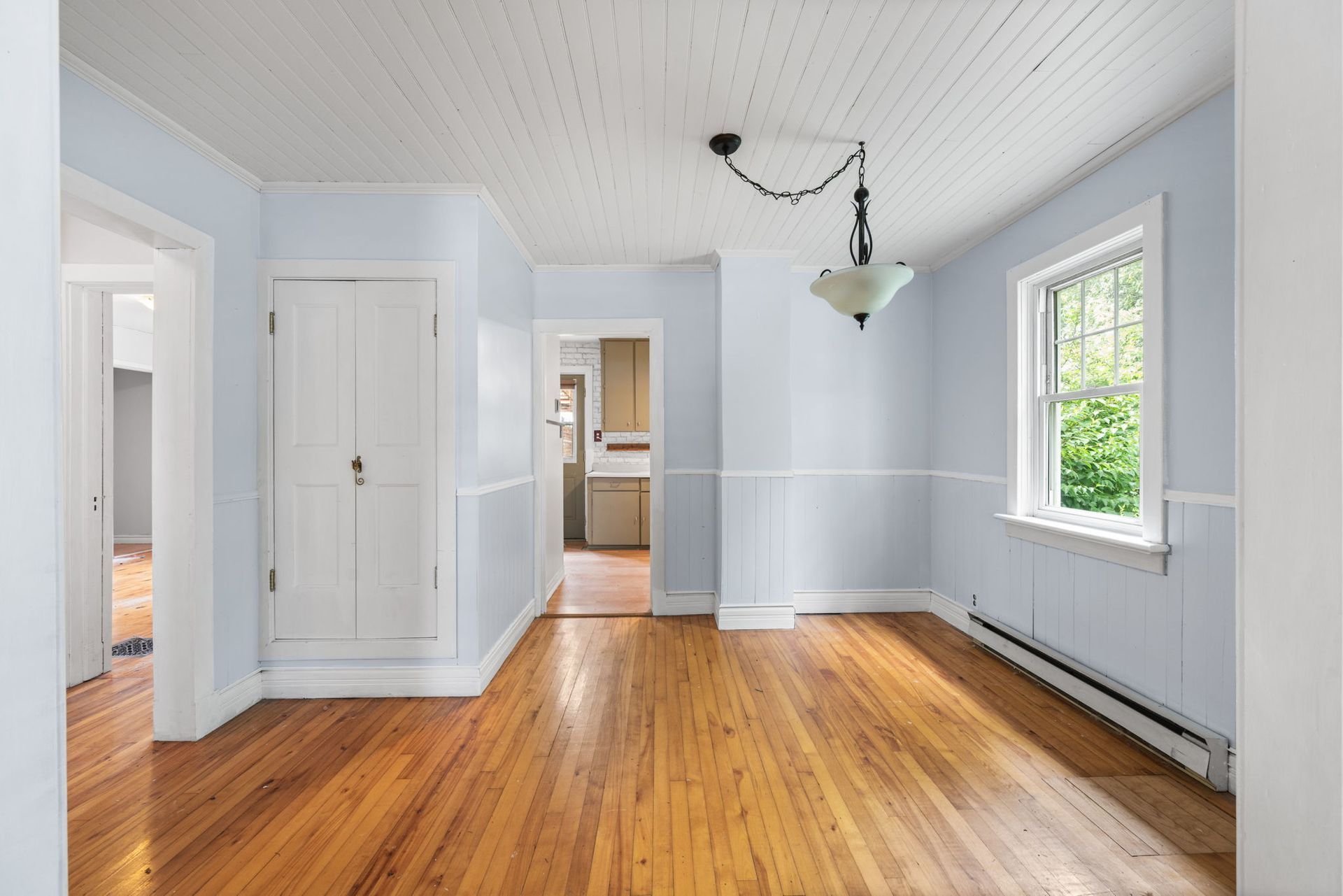 Empty room with wood floors, light blue walls, and white wainscoting and ceiling.