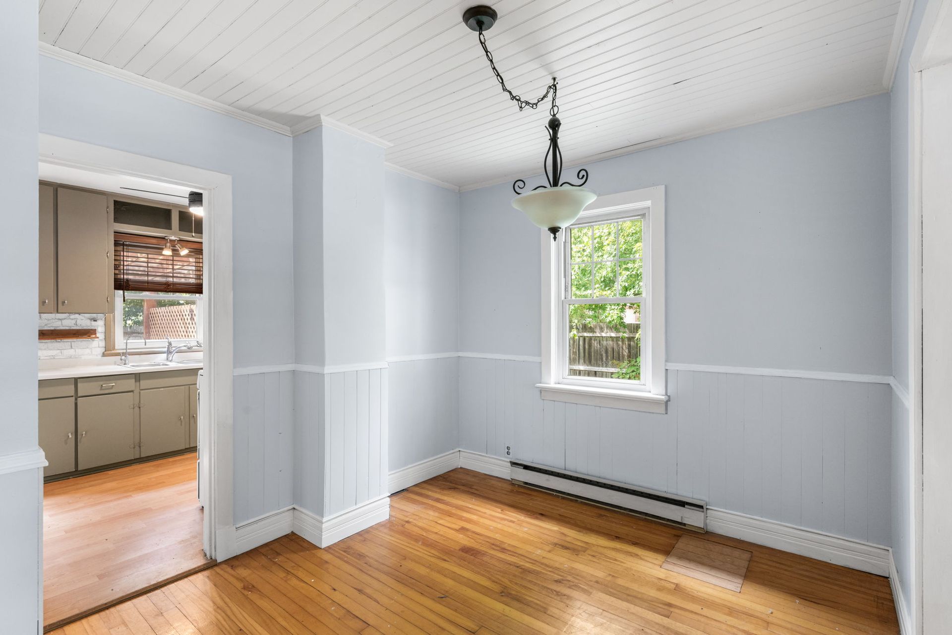 Empty dining room with blue walls, wood floor, white trim, and a view into a kitchen.
