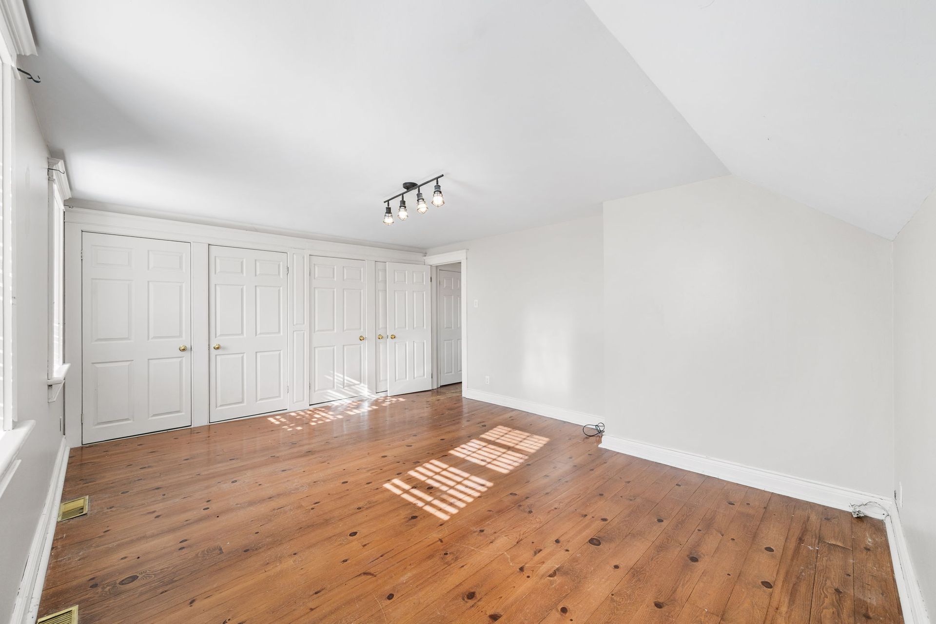 Empty bedroom with wooden floor, white walls, built-in closet, and a ceiling light.