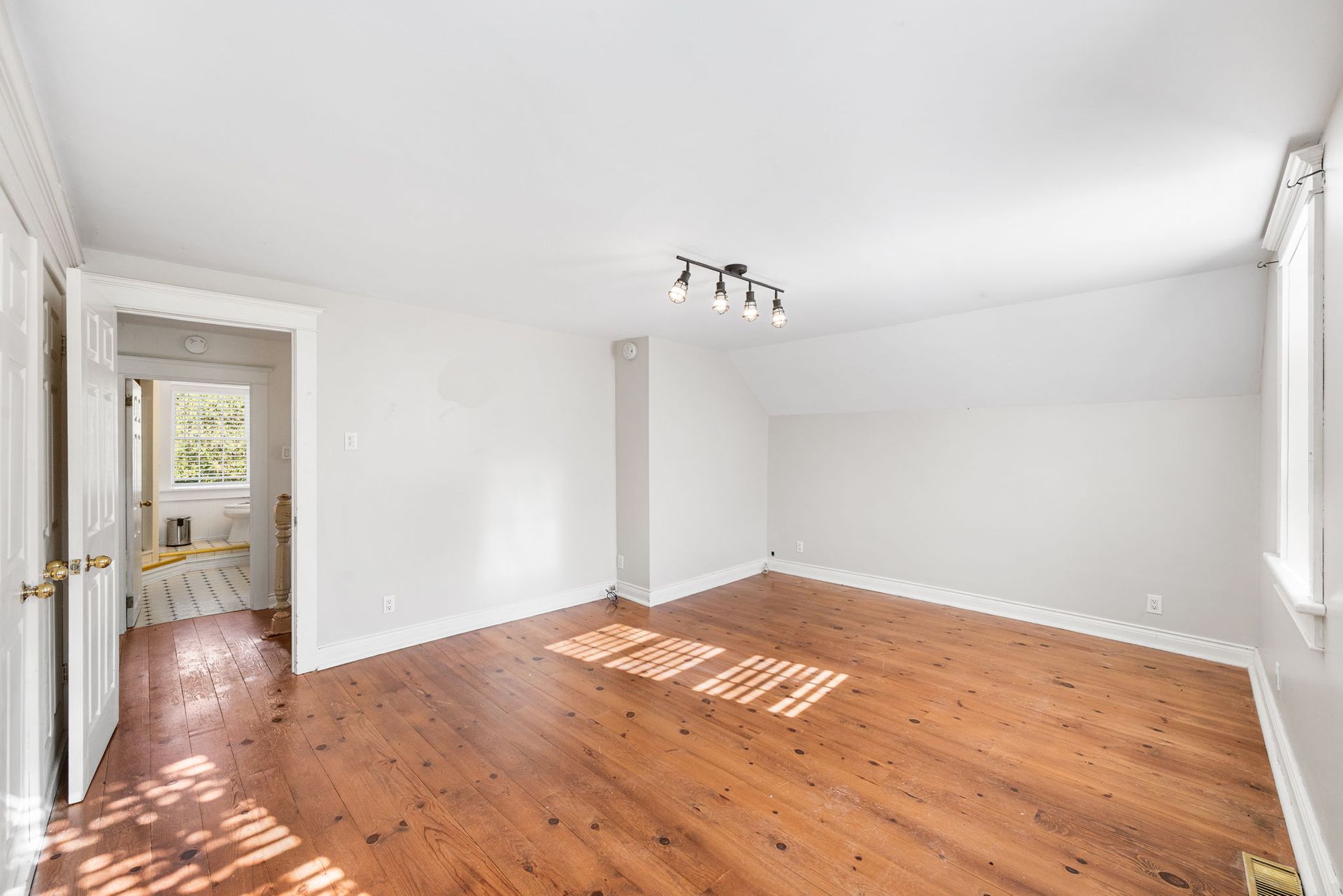 Empty bedroom with wood floors, white walls, and a doorway to another room.