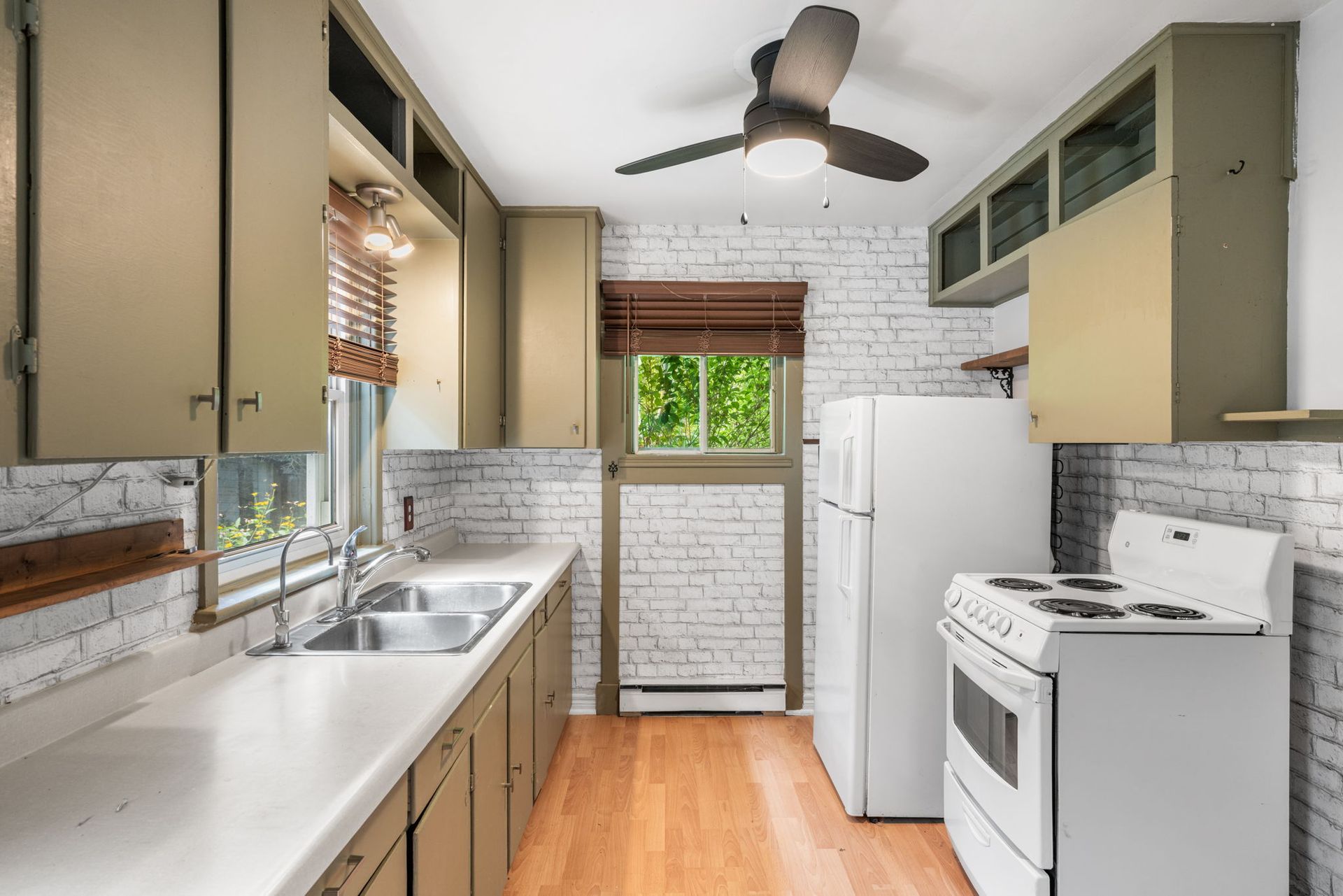 Kitchen with white brick walls, green cabinets, white appliances, and wood floors.
