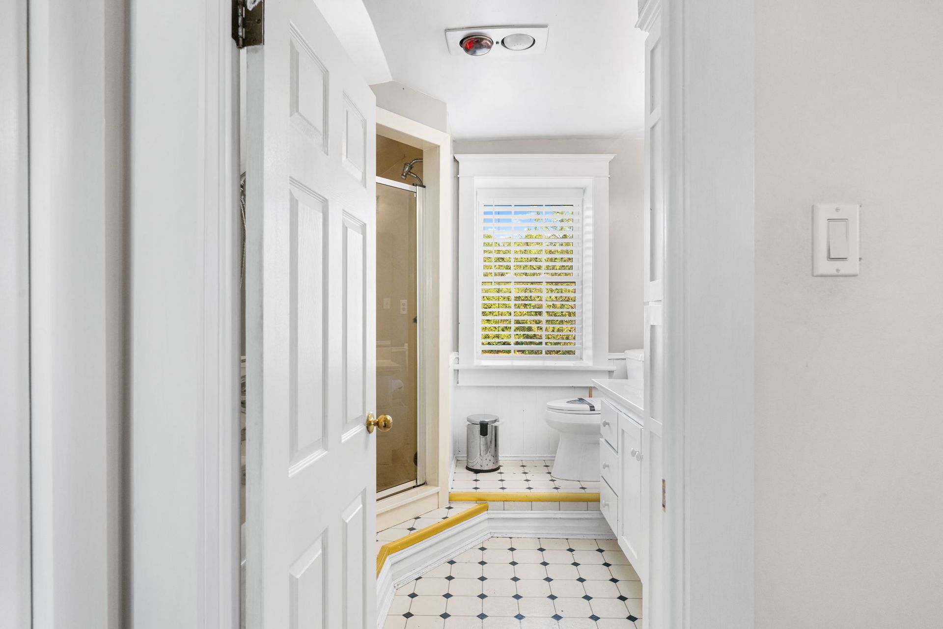 Bathroom interior with white walls, black and white tiled floor, shower, and window.