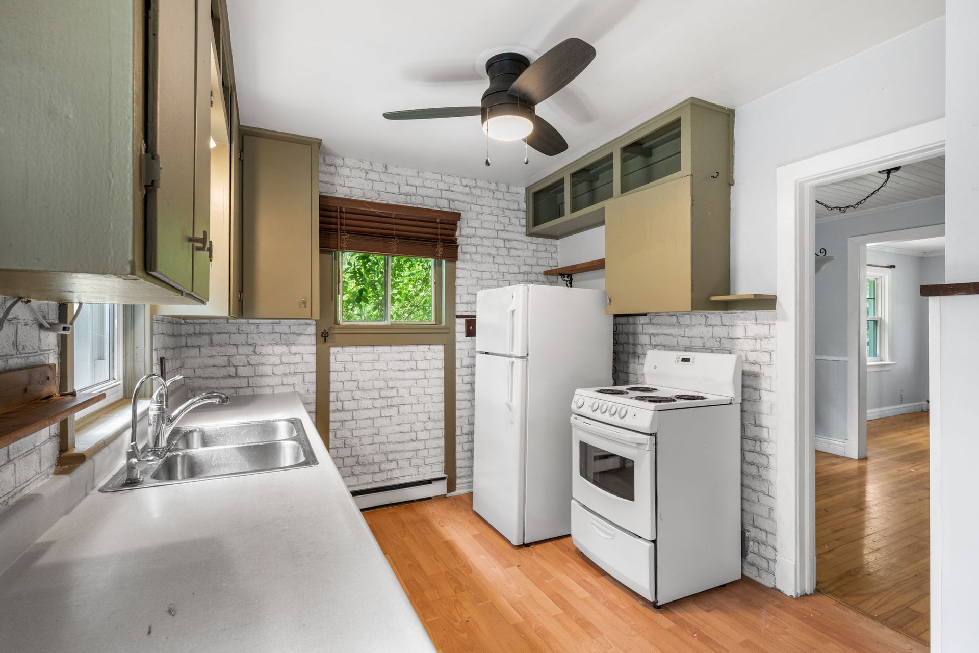 Kitchen with white appliances, exposed brick, sage green cabinets, and wood flooring.