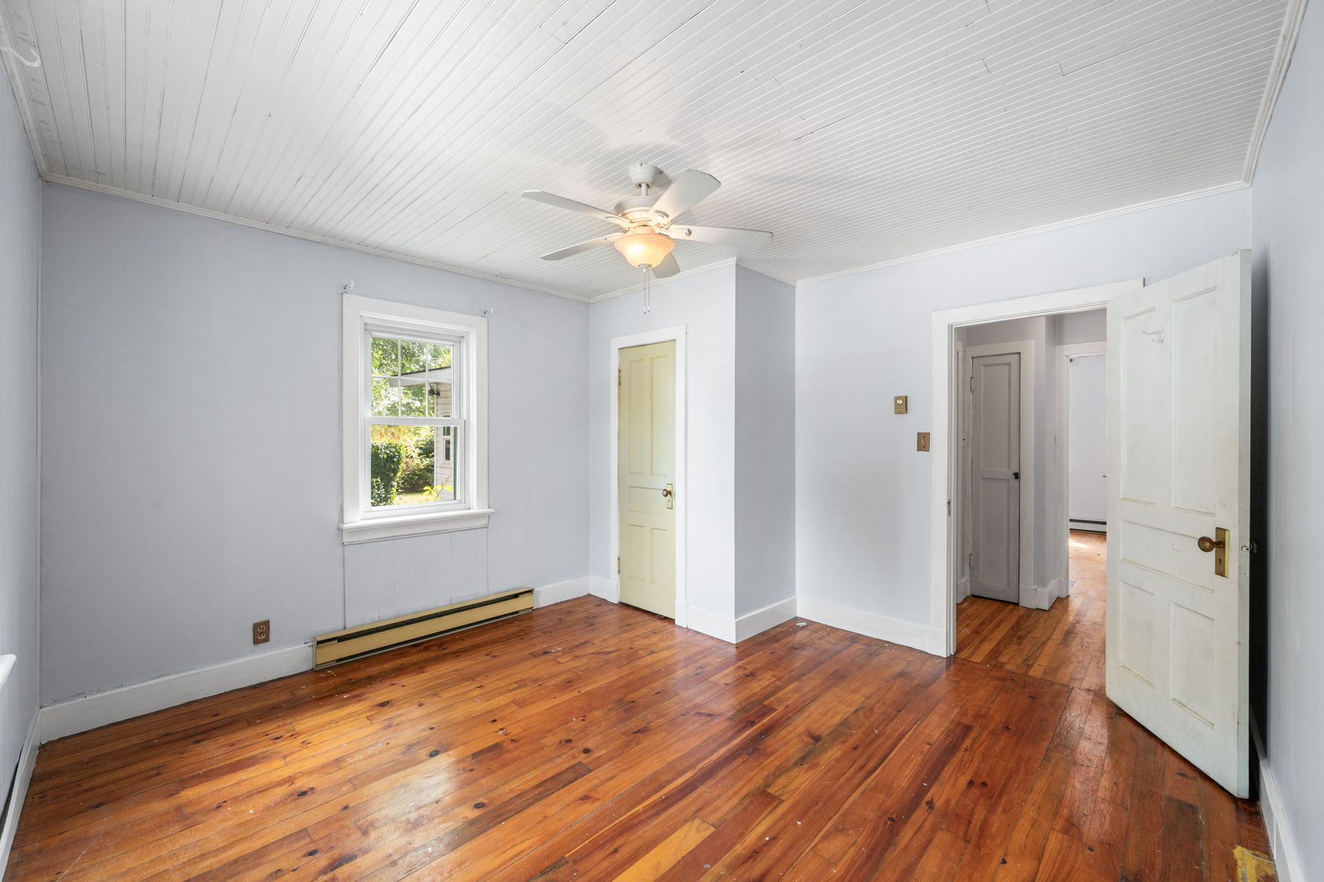 Empty bedroom with hardwood floors, light blue walls, and a white ceiling with a ceiling fan.