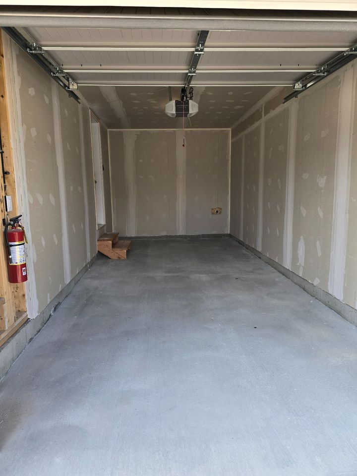 An empty garage with a garage door open and a fire extinguisher.